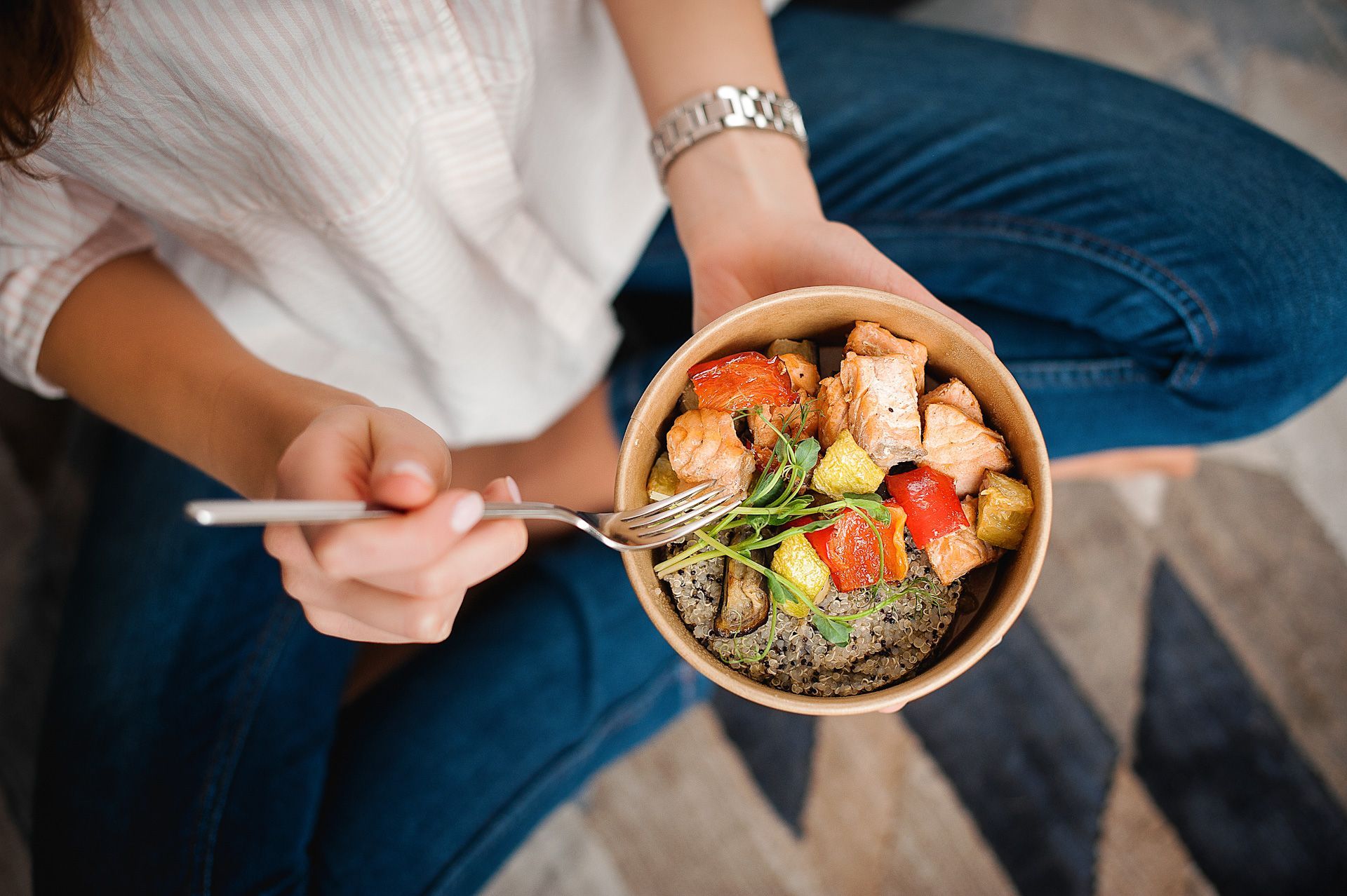 A woman is sitting on the floor eating a salad with a fork.