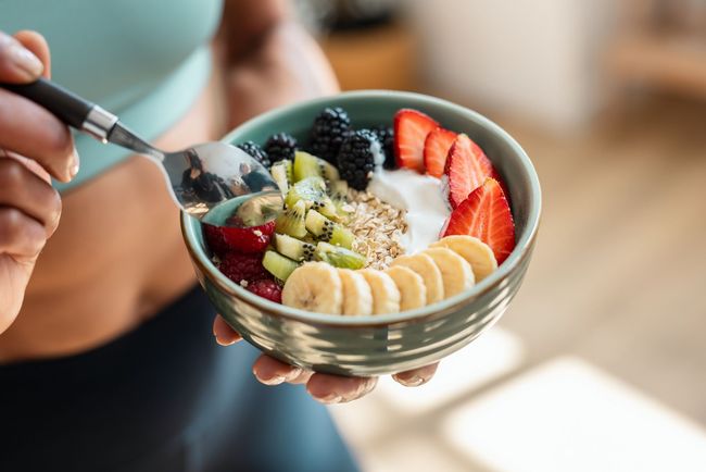 A woman is eating a bowl of fruit and yogurt with a spoon.