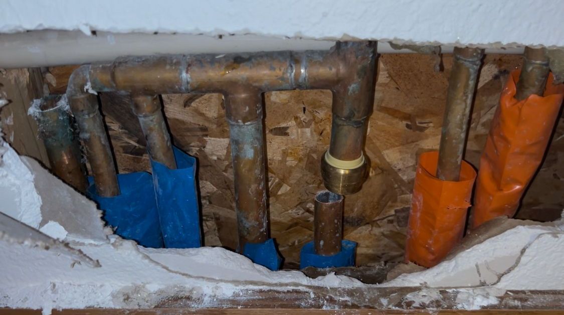 A hole in the wall with a bunch of pipes coming out of it.