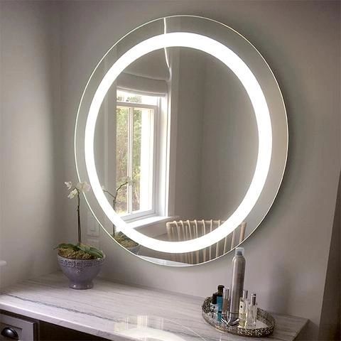A round mirror with a light around it is hanging on a wall in a bathroom.