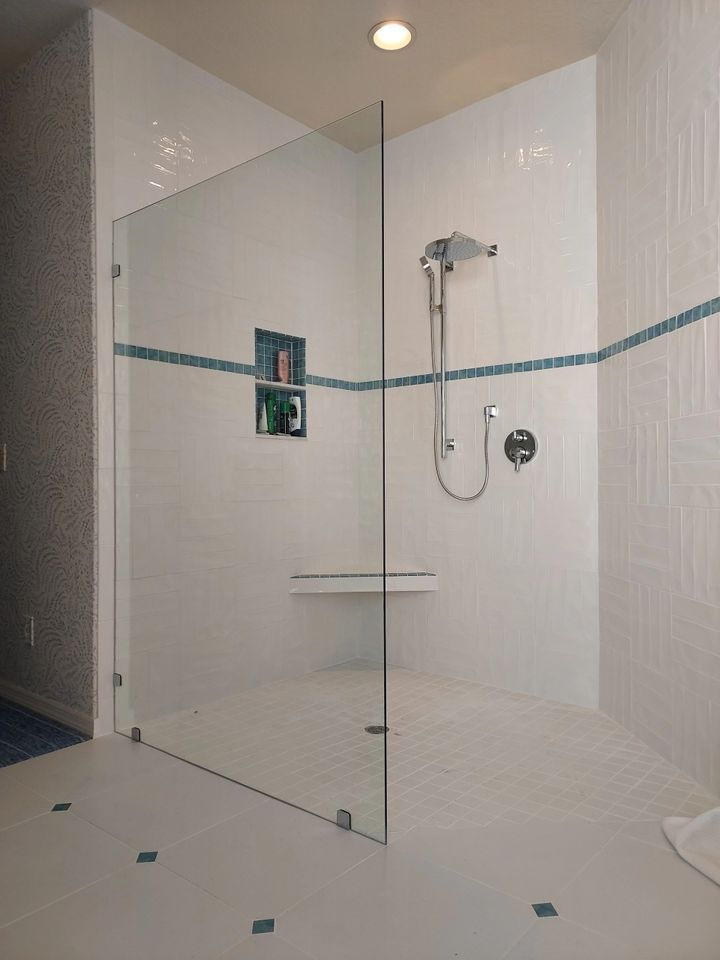 A walk in shower with a glass door and a bench.