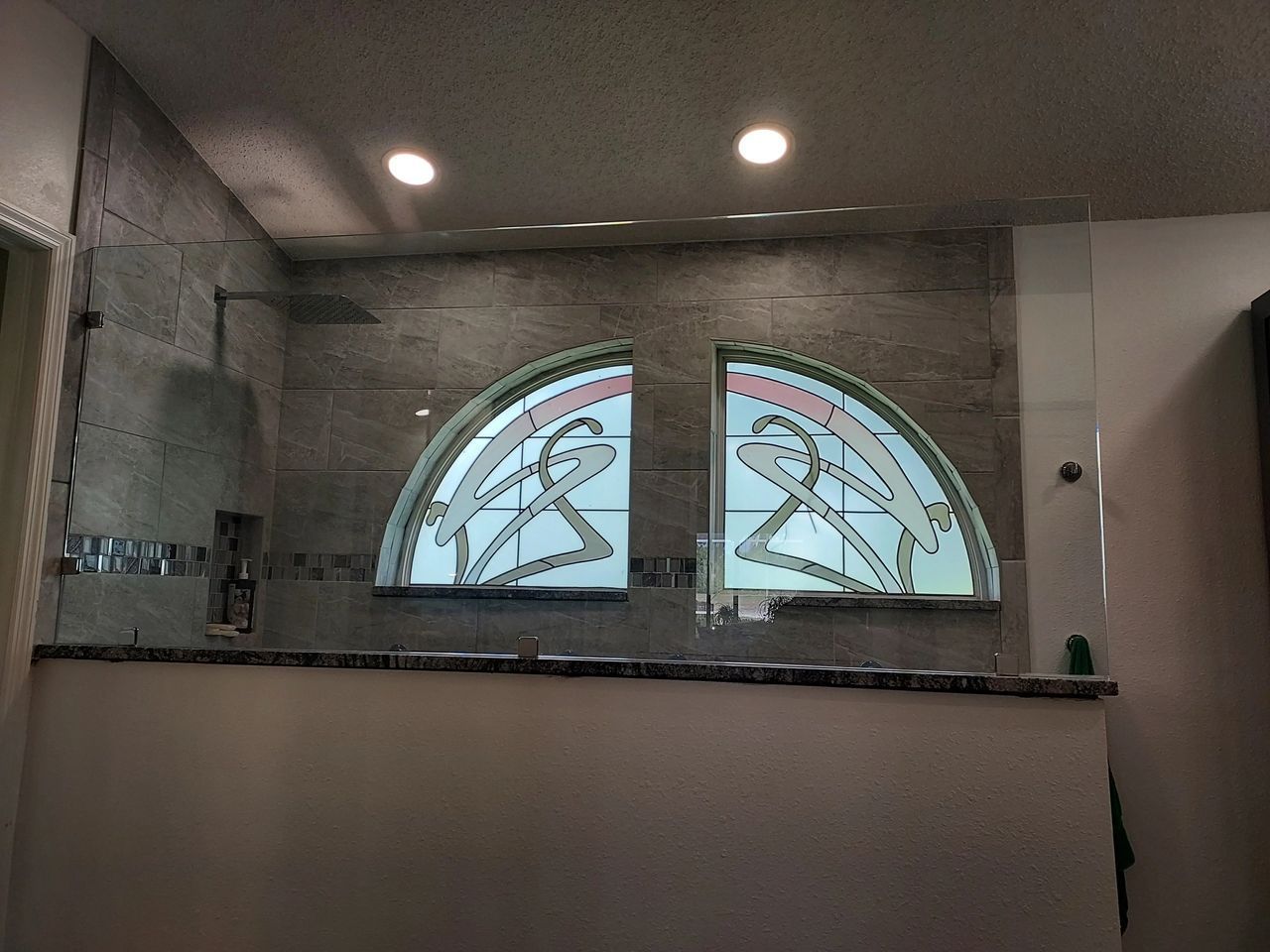 A bathroom with two arched windows and a shower stall.