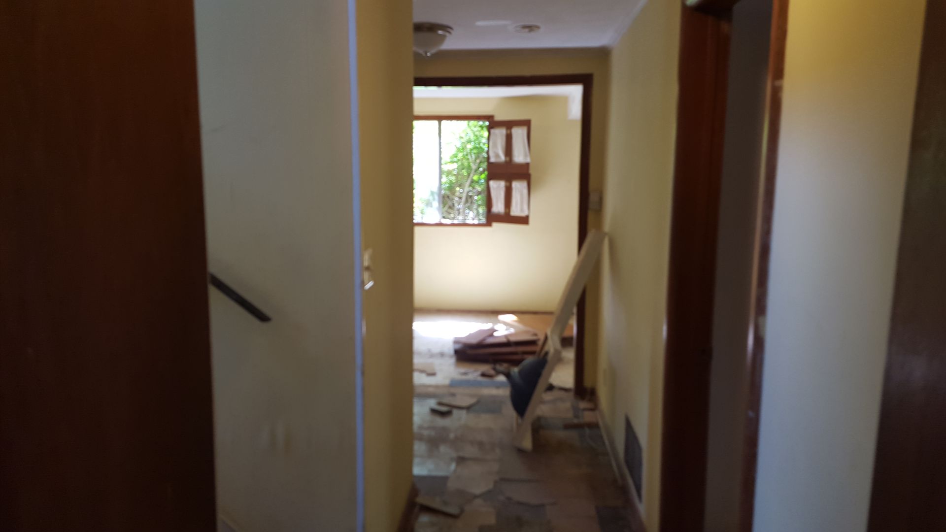 A narrow hallway with a stone-tiled floor leads to an empty room with a window and construction materials on the floor.
