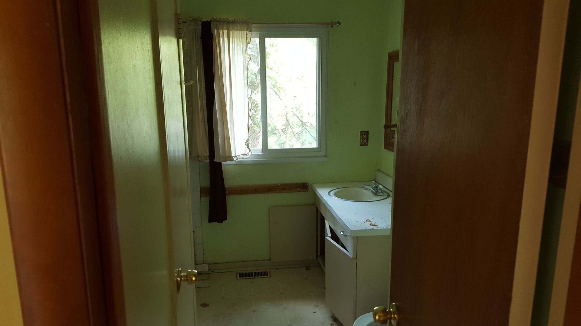 A doorway opens to a sparse bathroom with mint green walls, a window with curtains, and a white sink vanity.