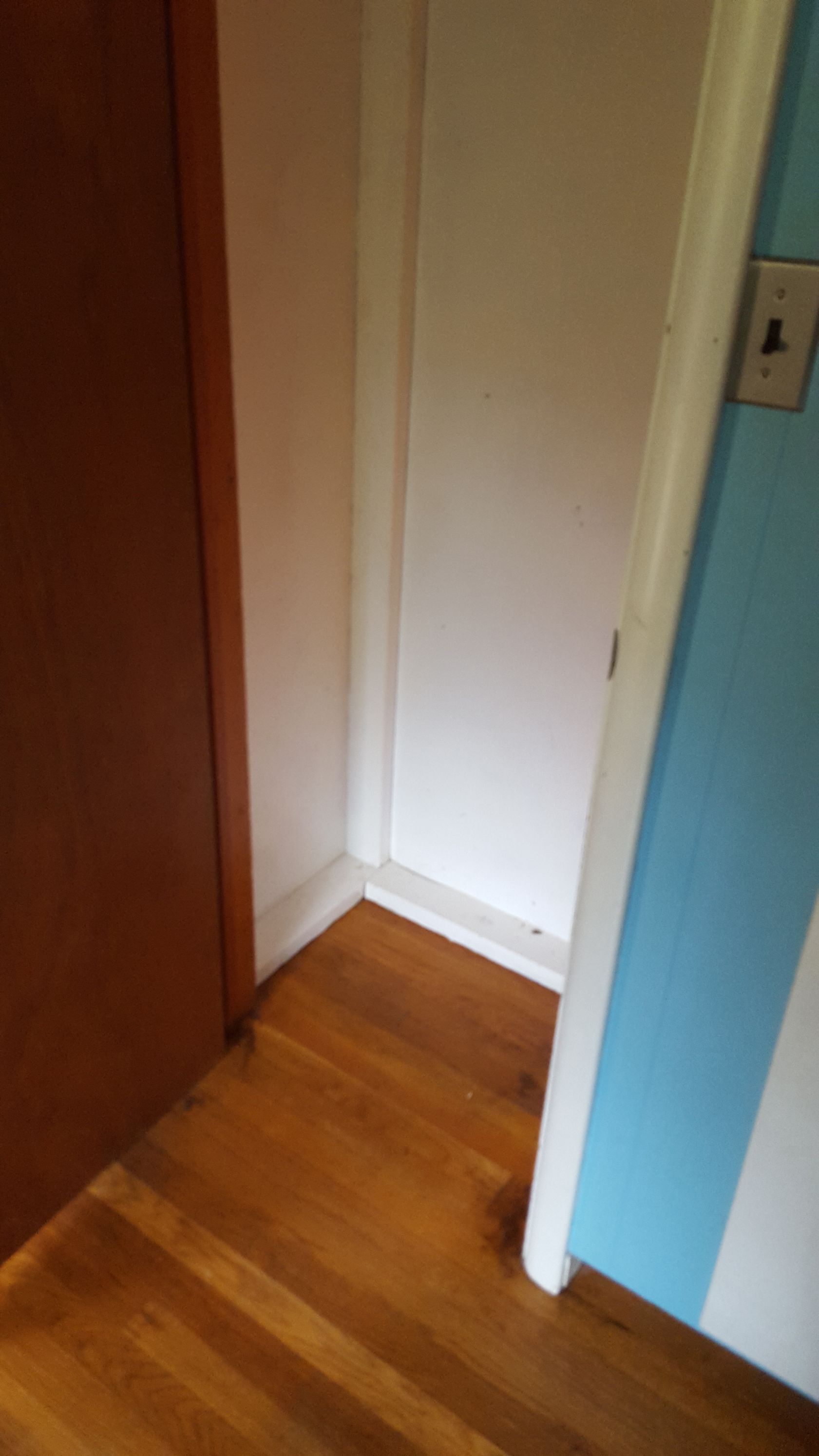 A narrow doorway with white trim and a white door, situated between a dark wooden door on the left and a blue wall.
