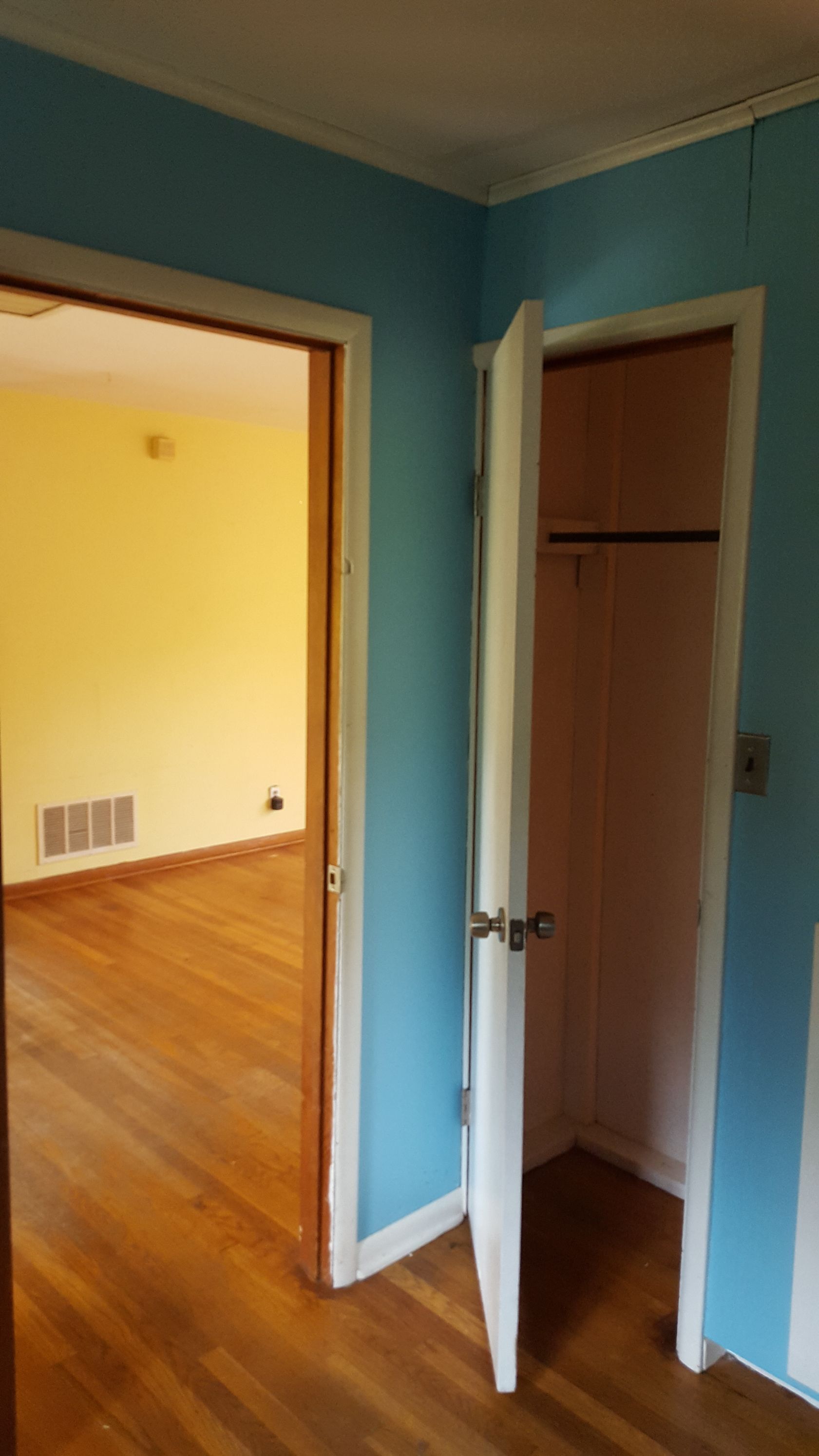 A hallway with blue walls featuring an open closet door on the right and an open doorway to a yellow-walled room ahead.