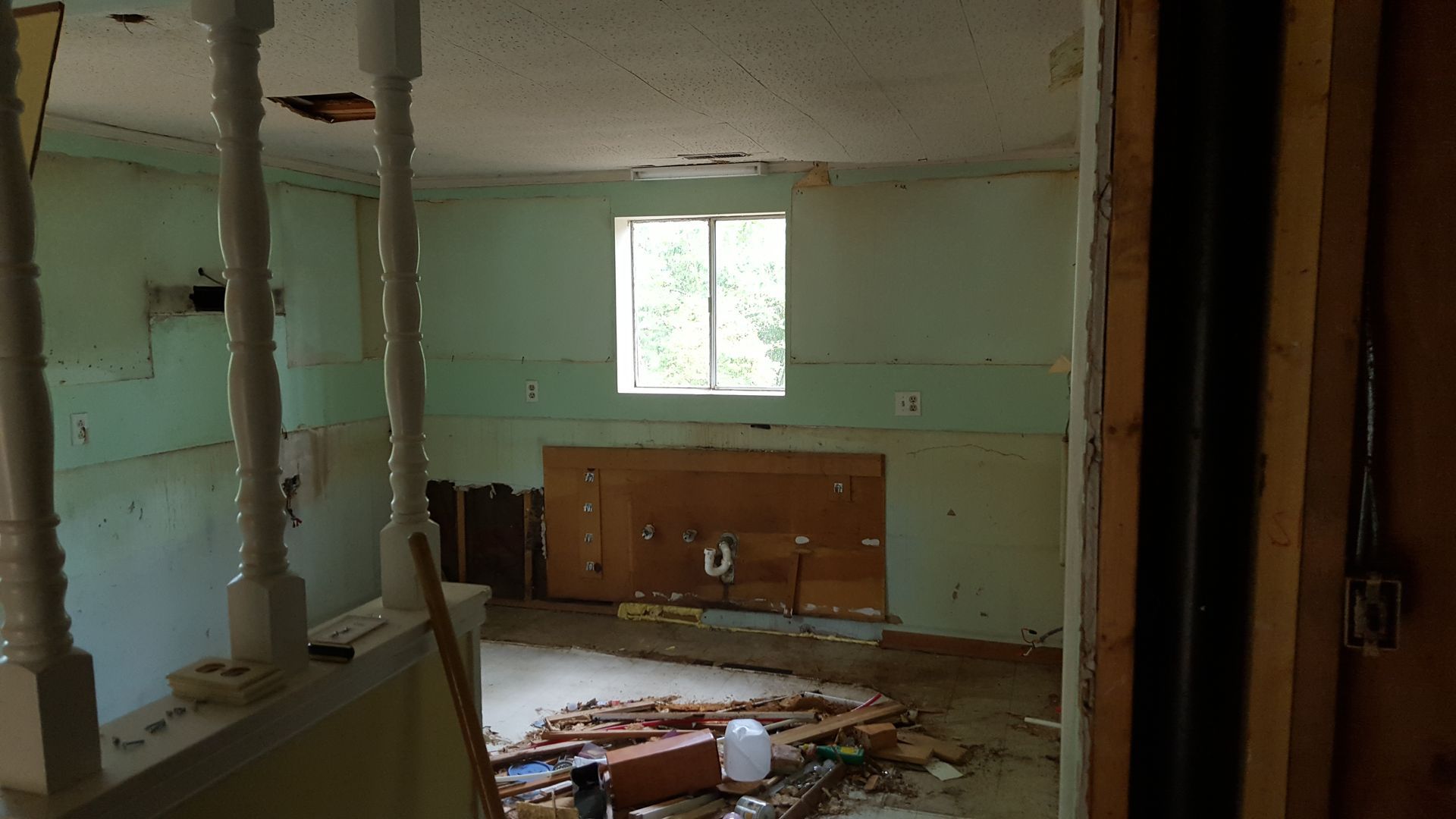An interior view of a room under renovation with exposed wall studs, debris on the floor, and two white decorative pillars.