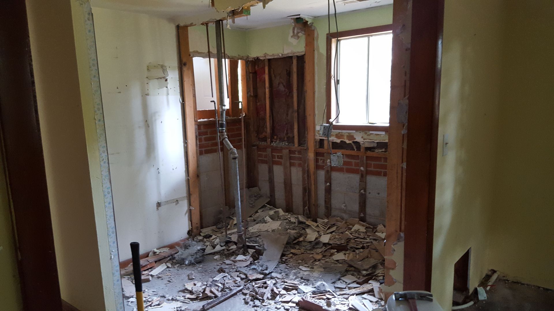 An interior room undergoing demolition, showing exposed wooden wall studs, brickwork, and debris scattered on the floor.