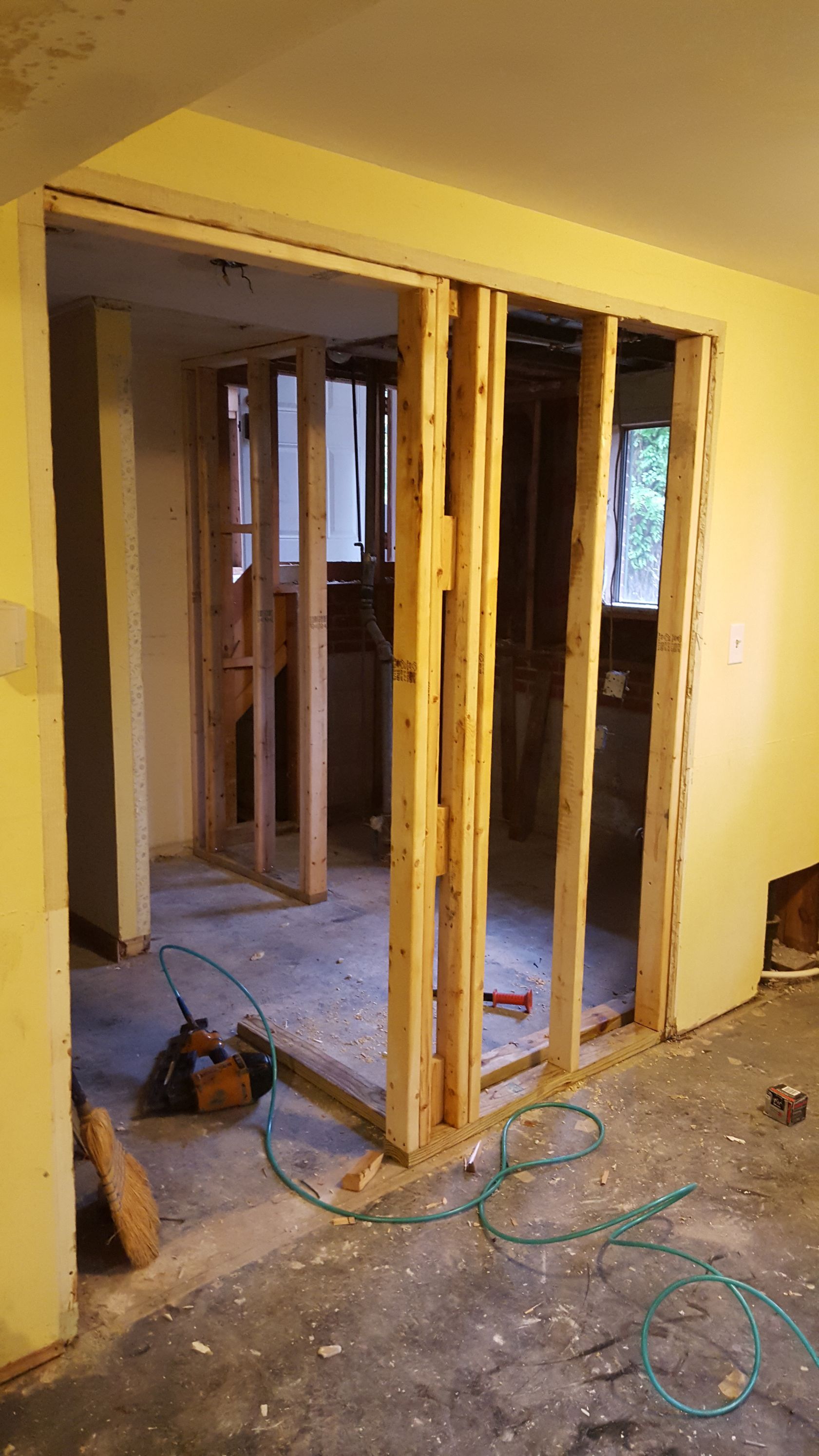 A newly framed doorway in a light yellow interior wall, revealing a partially renovated room with wooden studs.