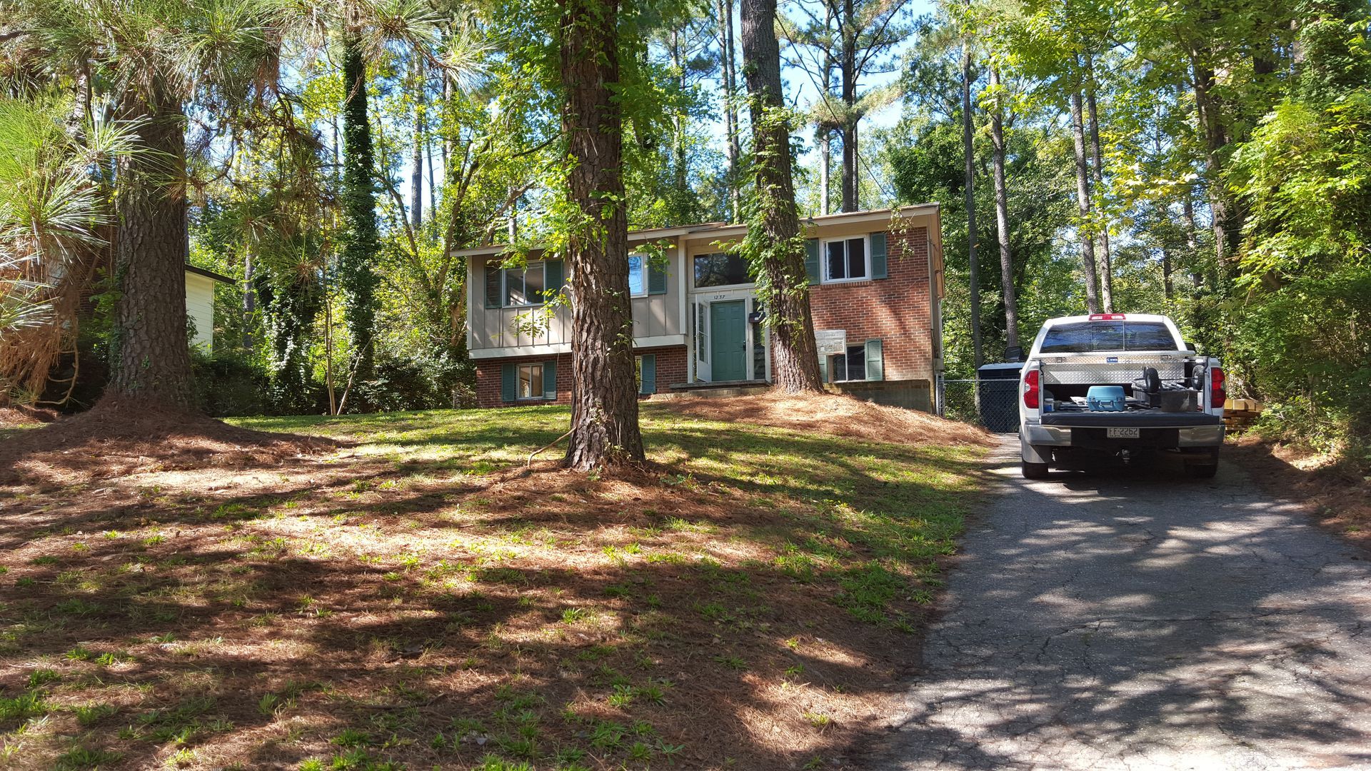 A brick split-level house surrounded by pine trees with a pickup truck parked in the driveway.