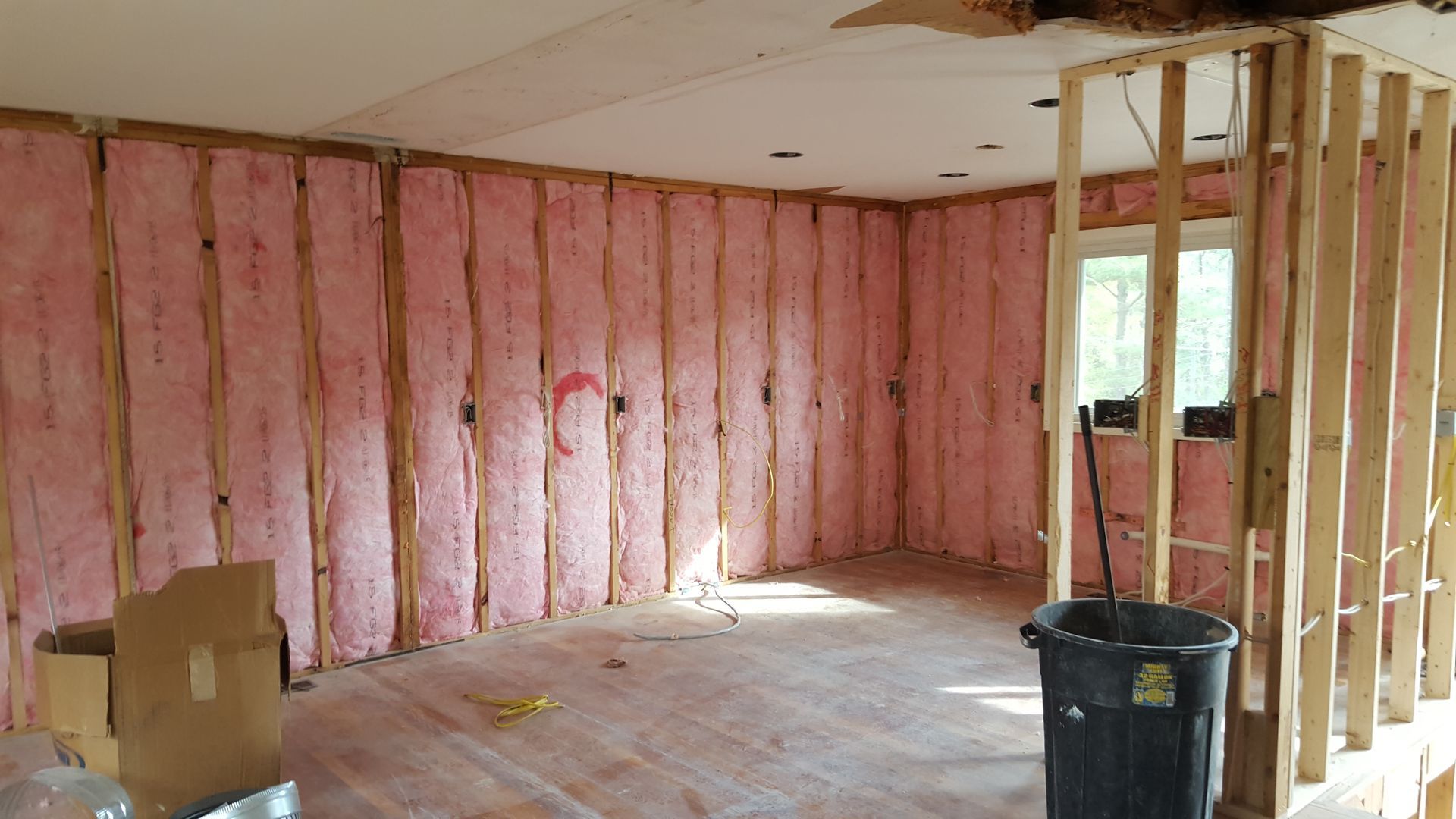 Interior view of a room under renovation with pink fiberglass insulation installed between exposed wooden wall studs.