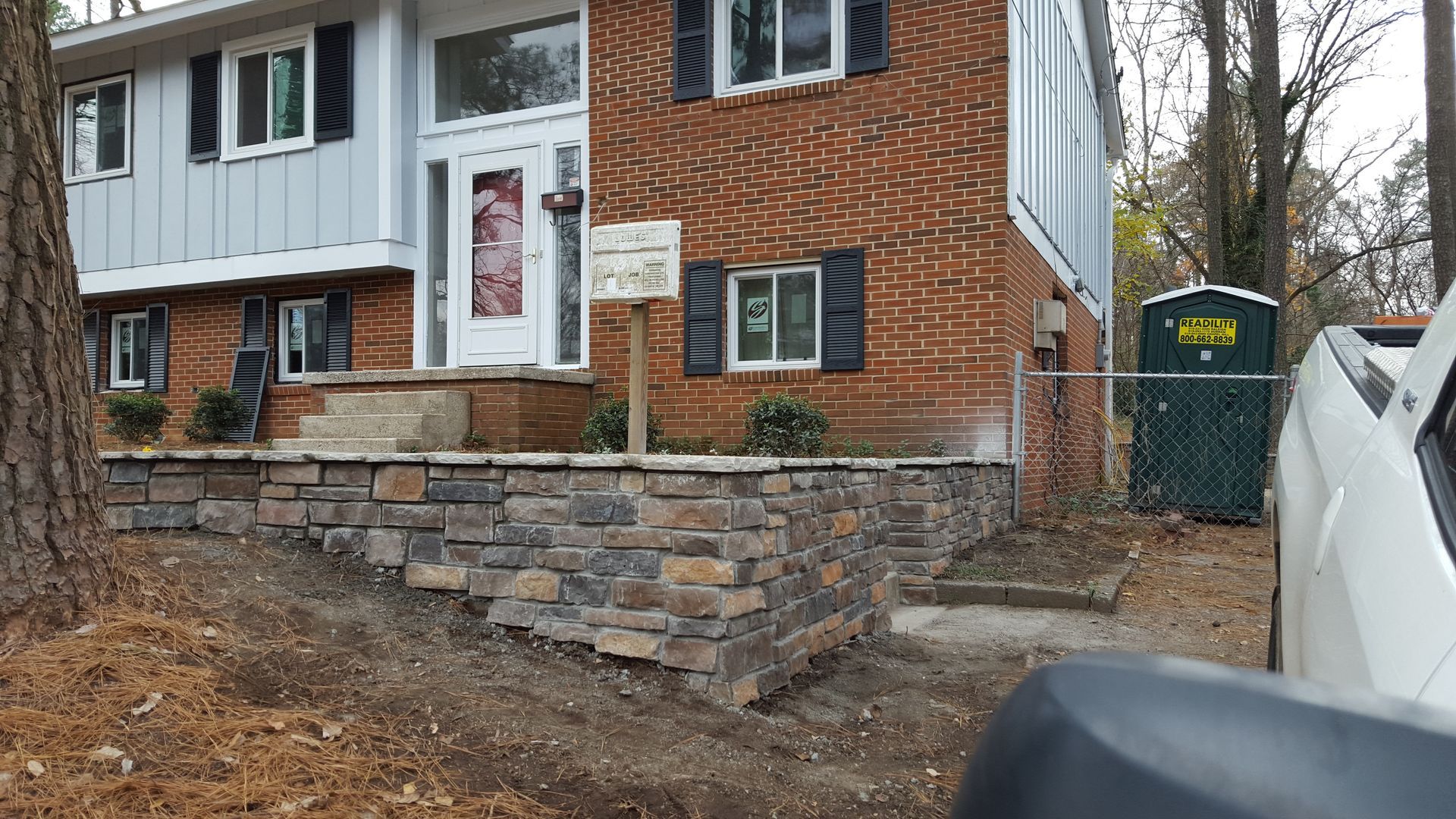 A split-level brick home with a newly constructed stone retaining wall and patio in the front yard.