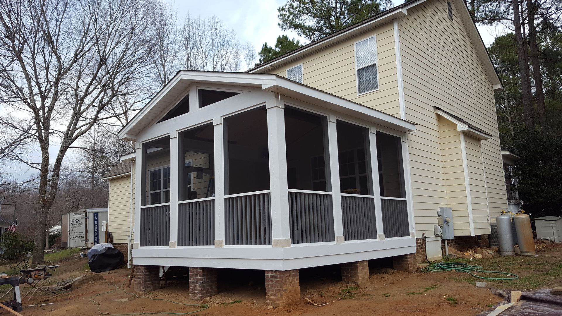 A cream-colored two-story house with a newly constructed, white-framed screened-in porch on a brick pier foundation.