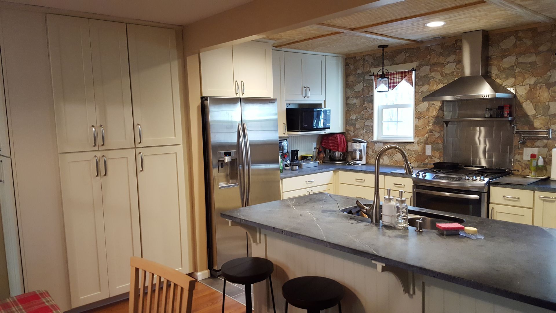 Kitchen with white cabinets, stone accent wall, stainless steel appliances, and a gray island with two stools.