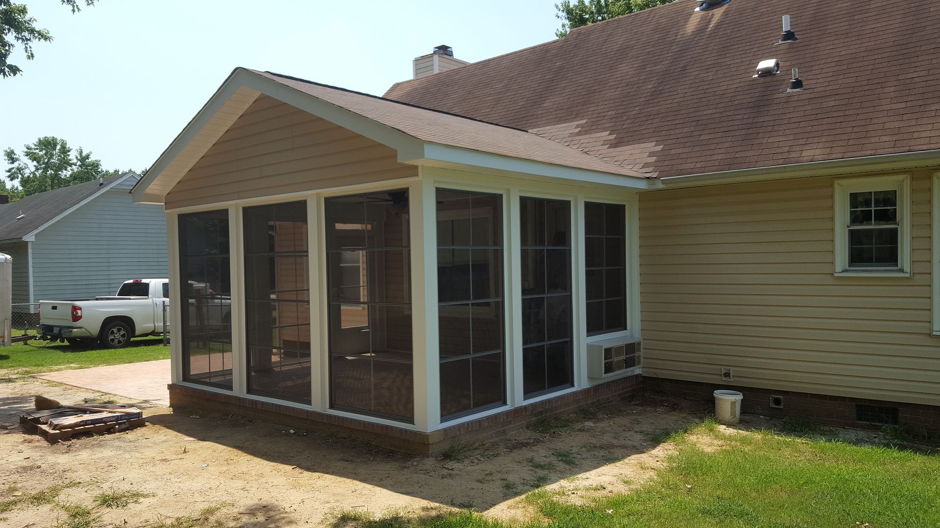 A tan house featuring a newly constructed screened-in porch with white trim and a brown gabled roof in a backyard setting.