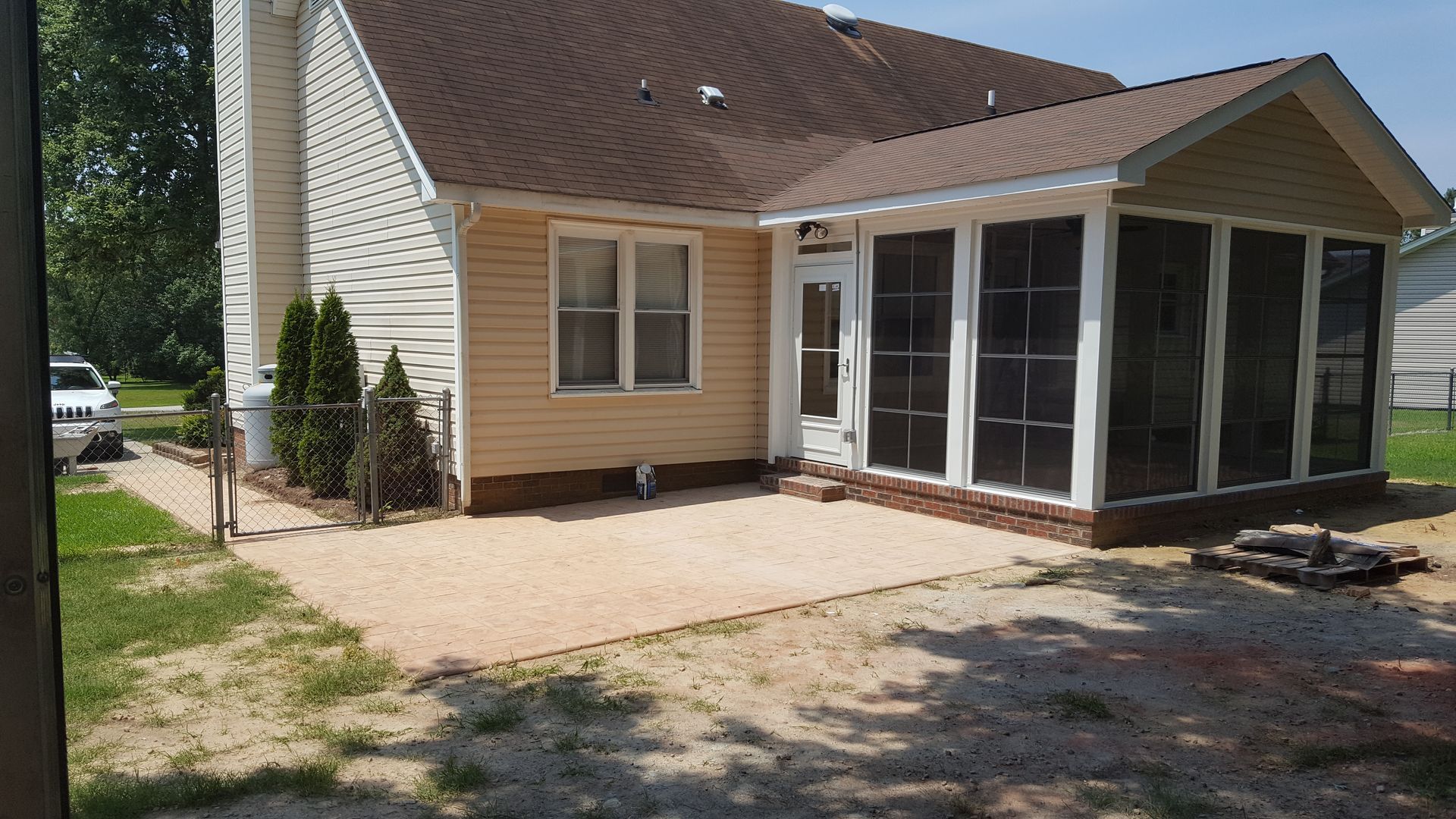A yellow siding house with a brick-foundation sunroom and an adjoining gravel patio in a residential backyard.