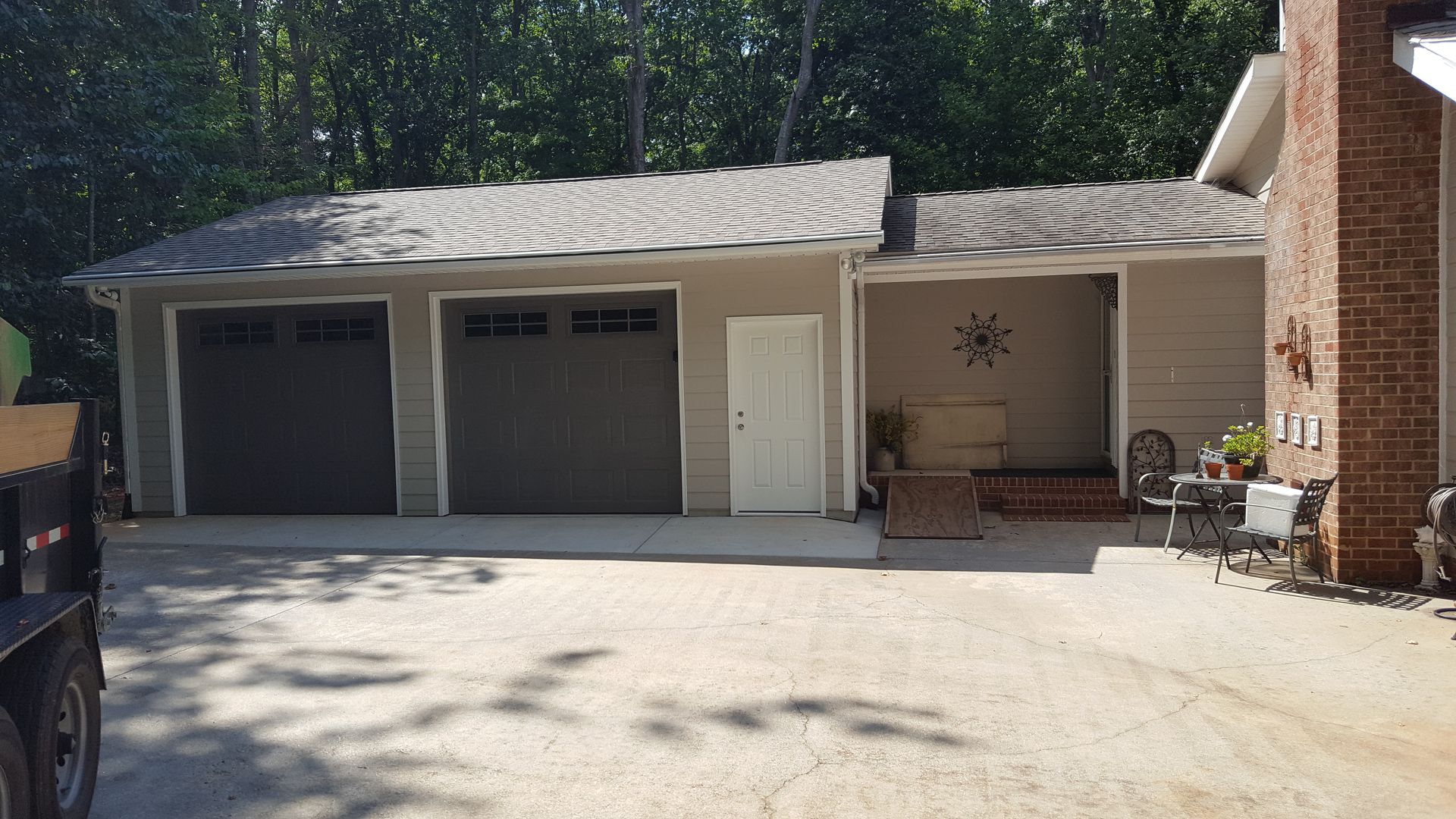 A house exterior with a two-car garage, a white entry door, and a covered patio area with outdoor furniture.