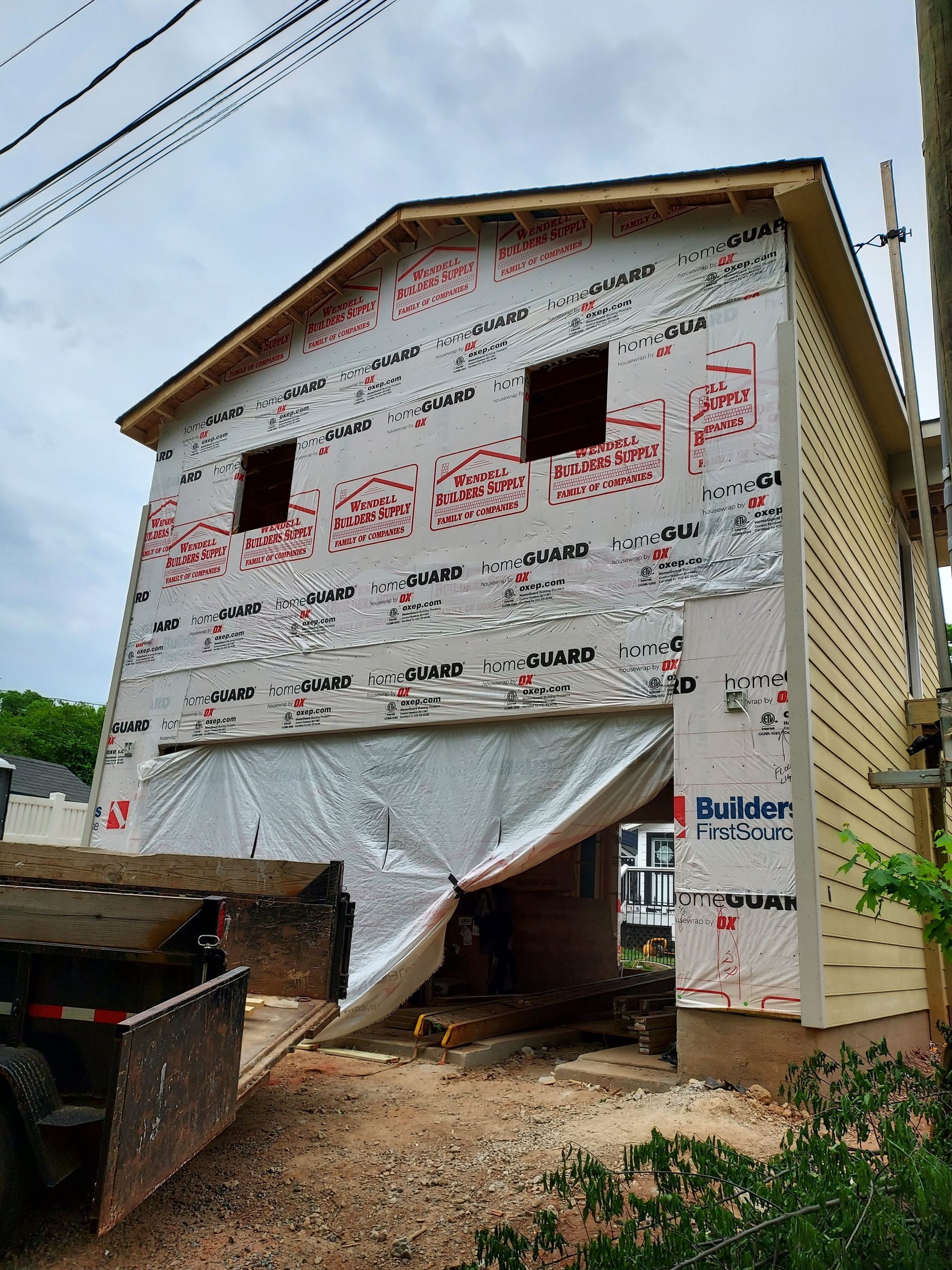 A two-story building under construction with exposed sheathing, a large open garage bay, and yellow siding on the side.