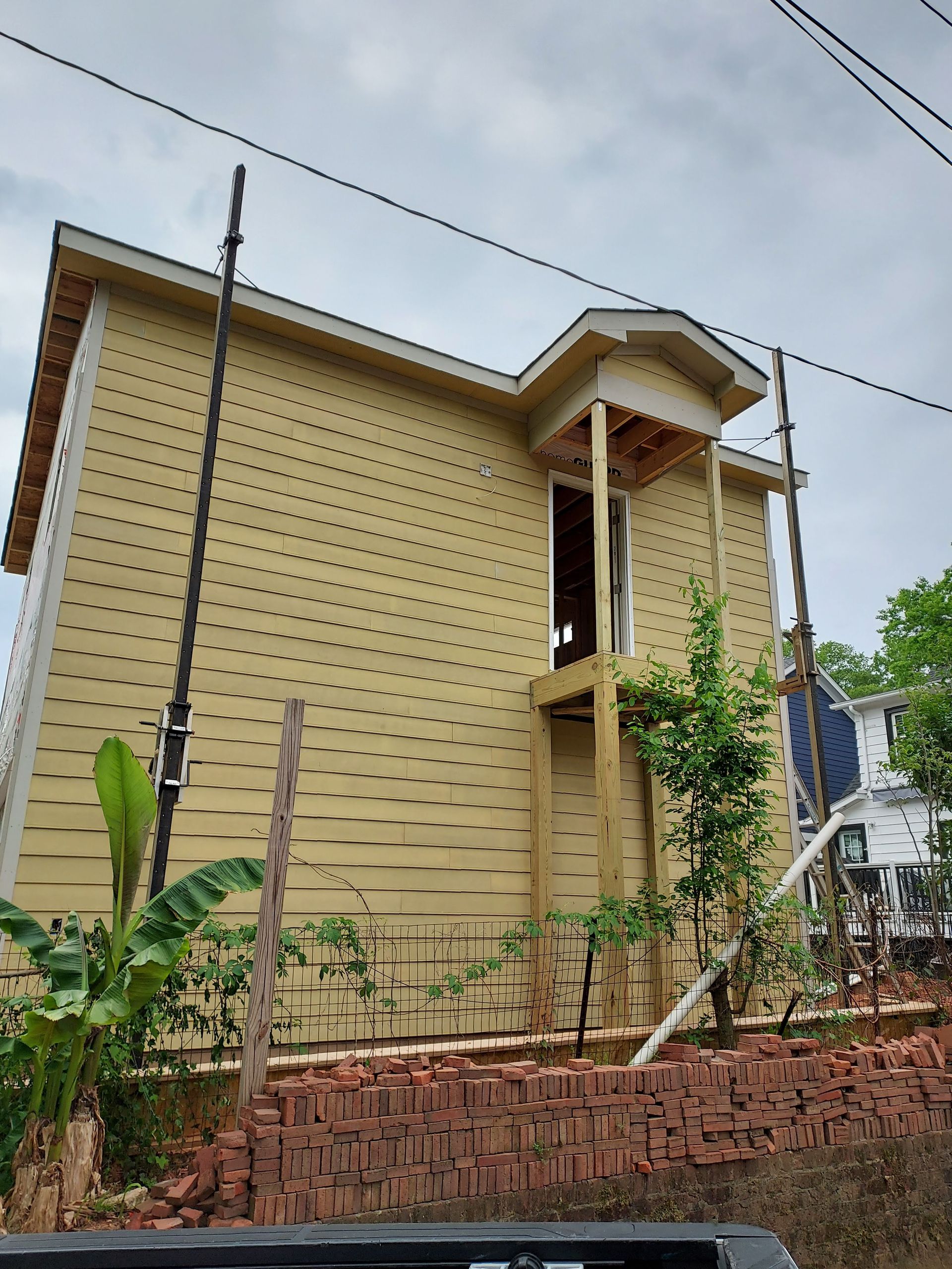 A two-story house with yellow siding features an unfinished wooden porch structure leading to an upper-level doorway.