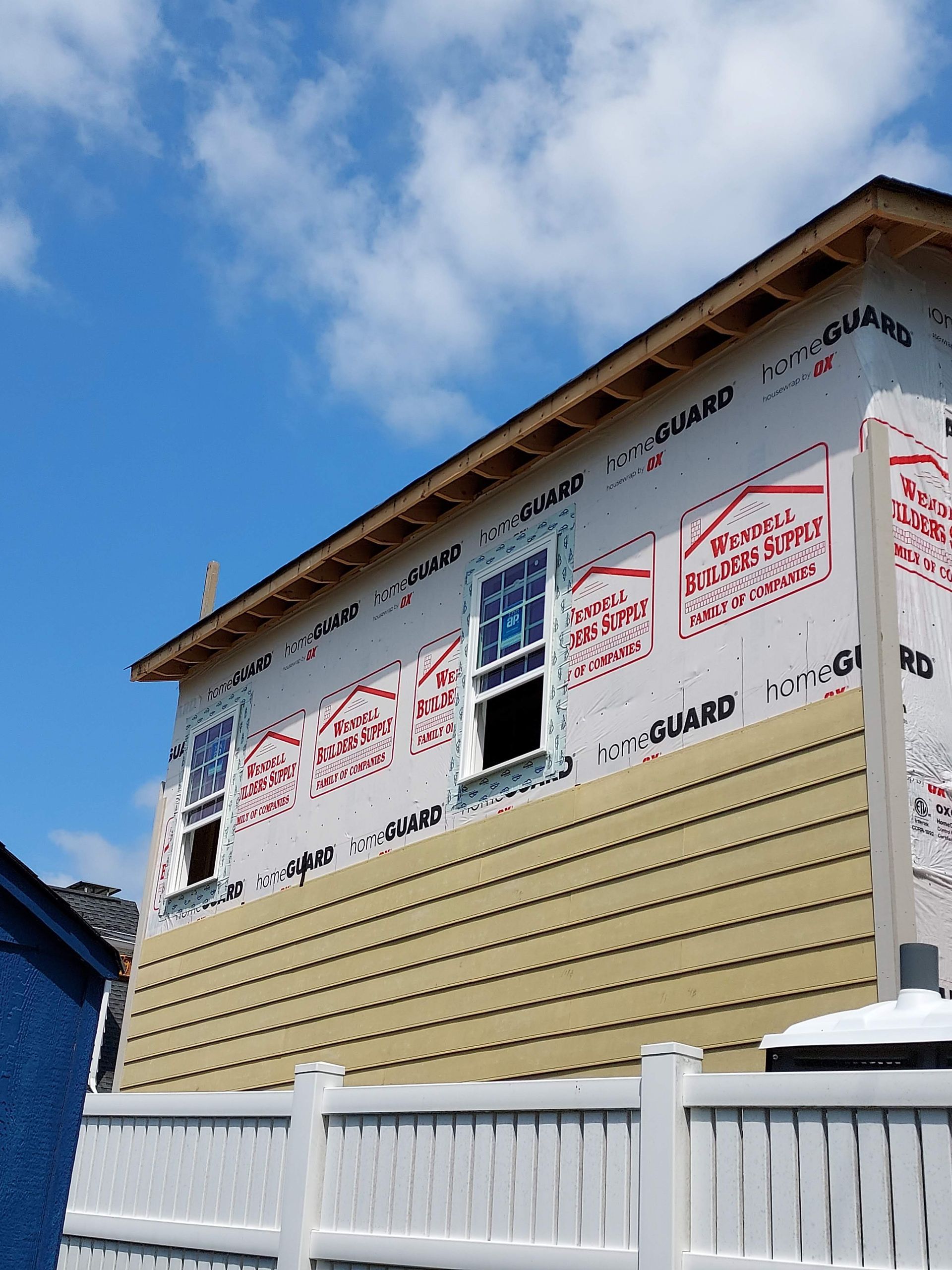 Exterior view of a two-story house under renovation, featuring tan lap siding partially installed over white house wrap.