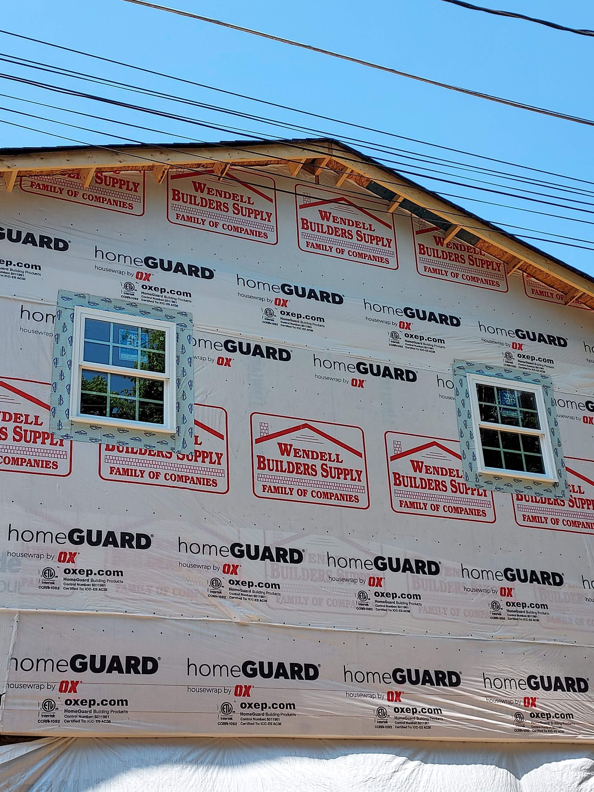 The upper exterior wall of a house under construction, covered in HomeGuard house wrap with two installed windows.