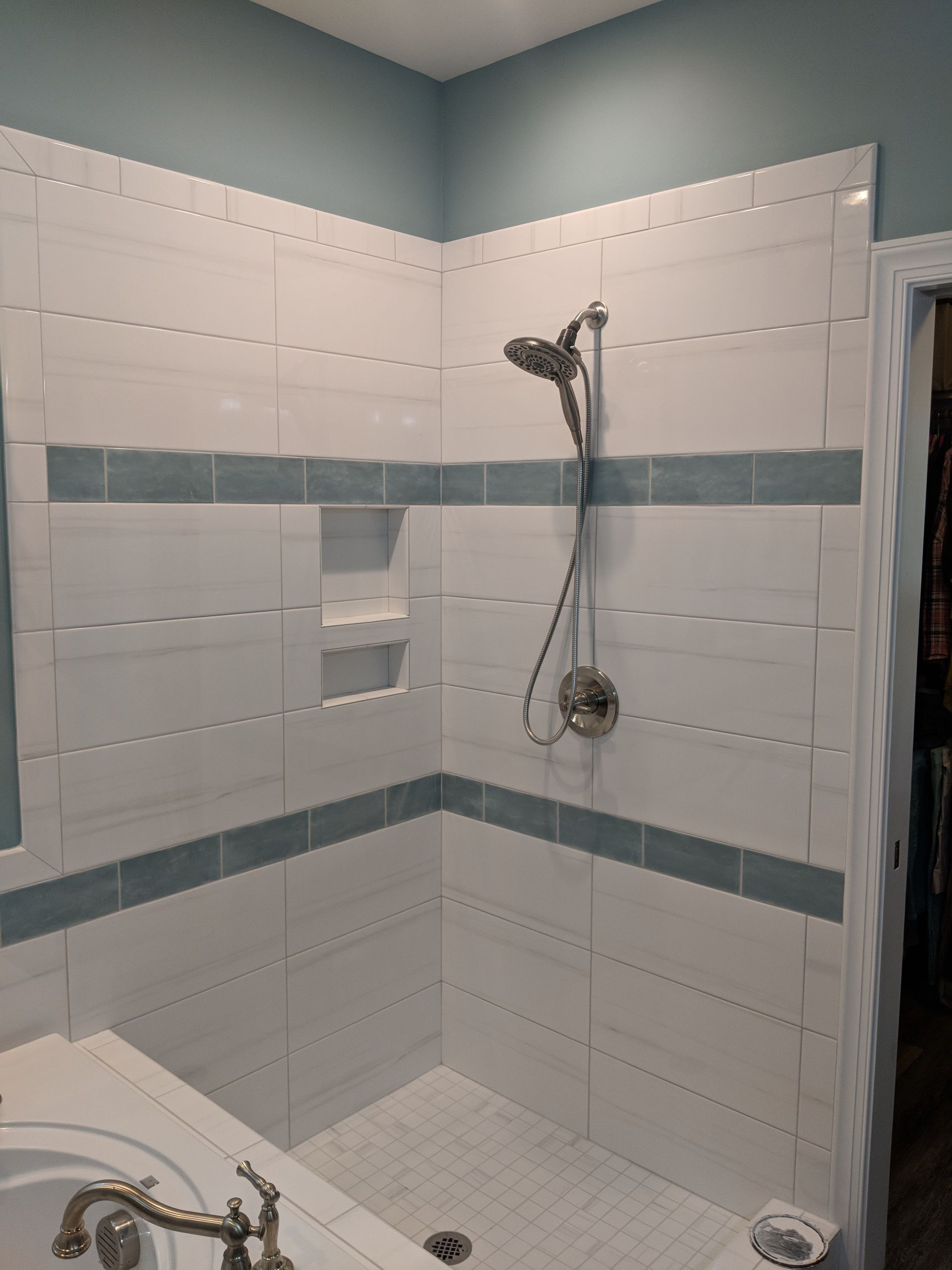 A tiled shower with white subway tiles, blue accent stripes, a silver handheld showerhead, and a built-in recessed niche.
