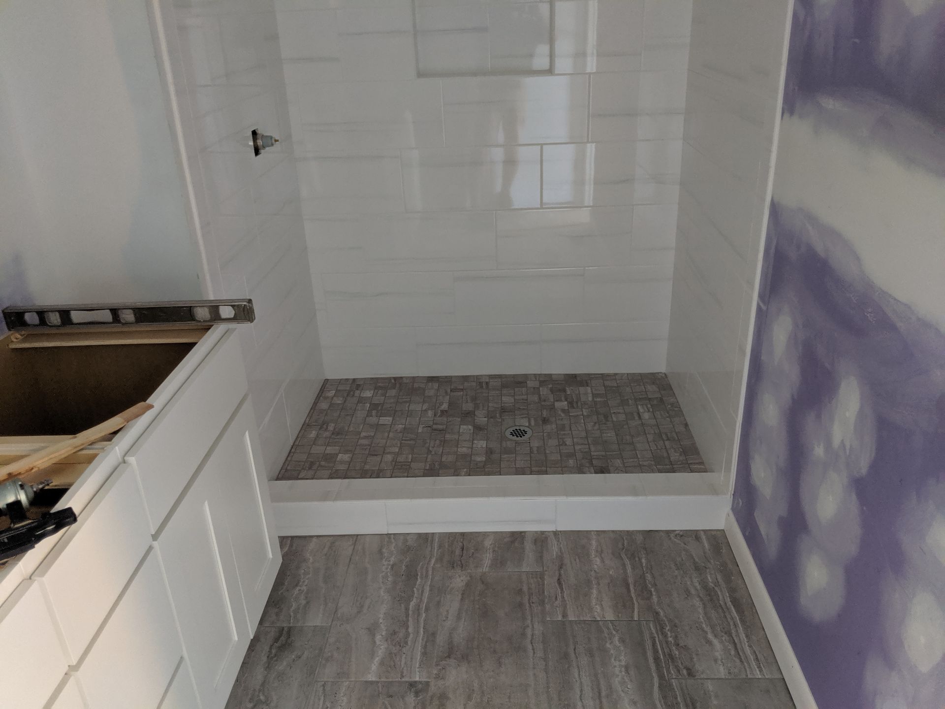 A bathroom renovation in progress, featuring a walk-in shower with white wall tiles, a stone floor, and a white vanity.