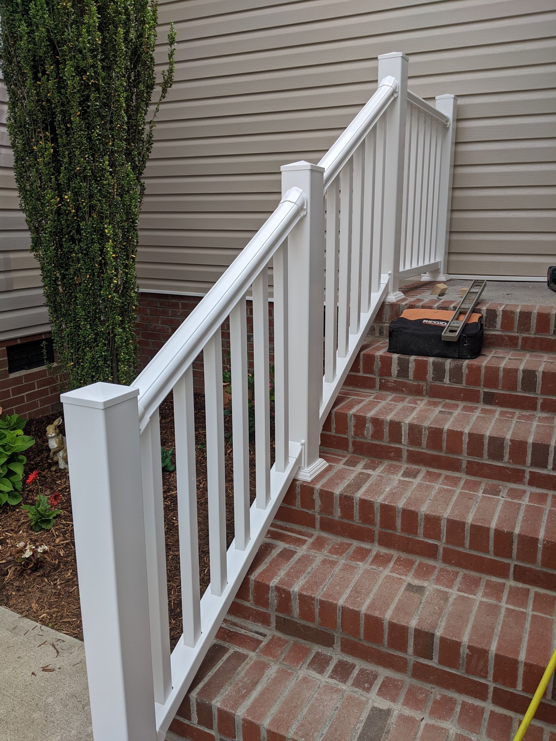 White vinyl handrail installed along red brick outdoor steps next to a house with beige siding.