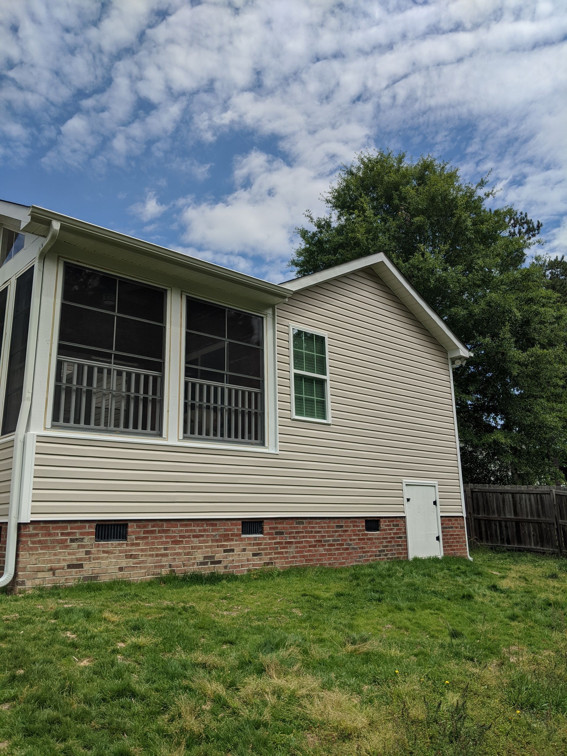 Side view of a one-story house with cream-colored siding, a brick foundation, screened porch, and a white access door.