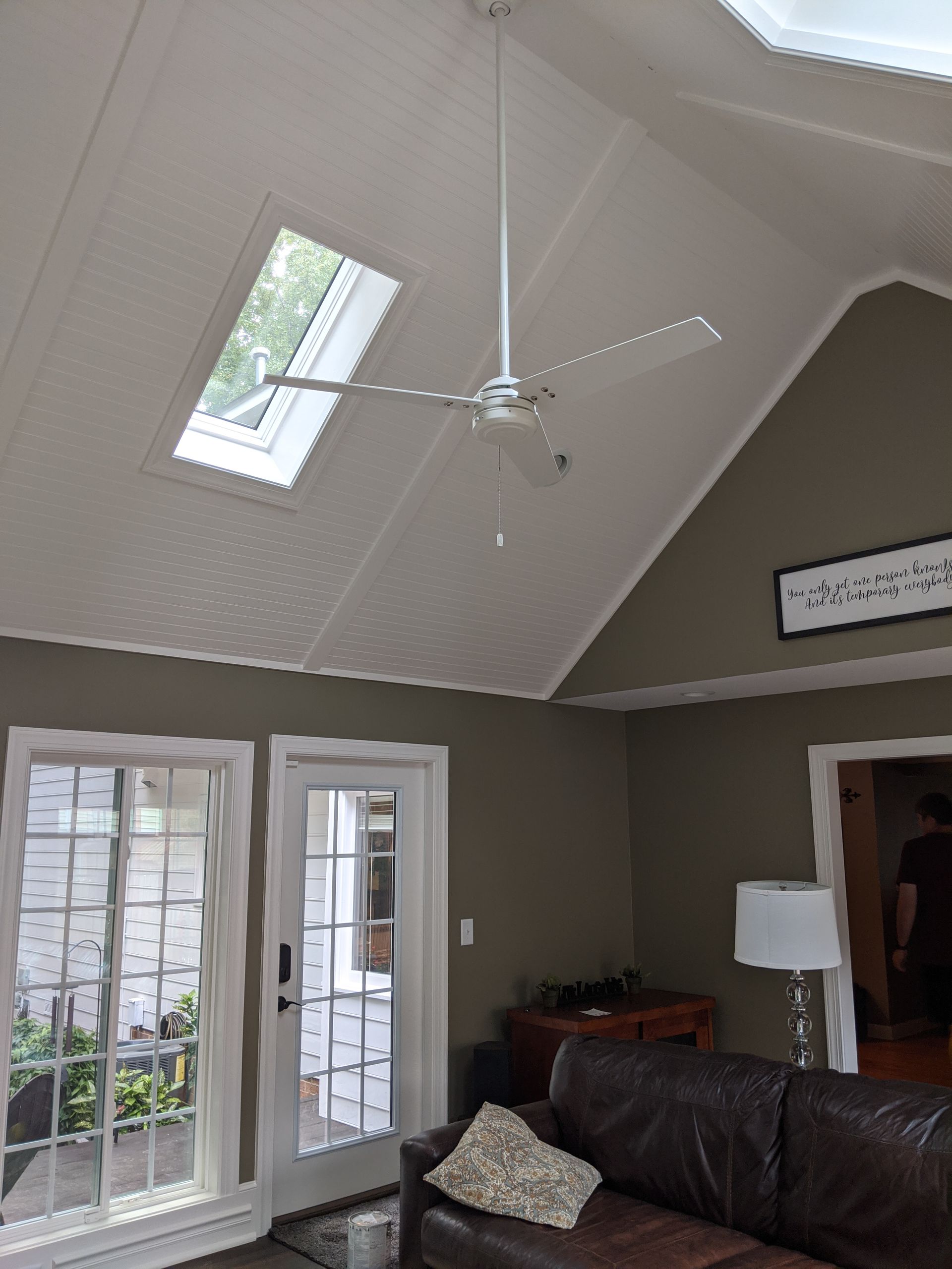 A living room with a high, vaulted ceiling, a skylight, a ceiling fan, dark olive walls, and a leather sofa.