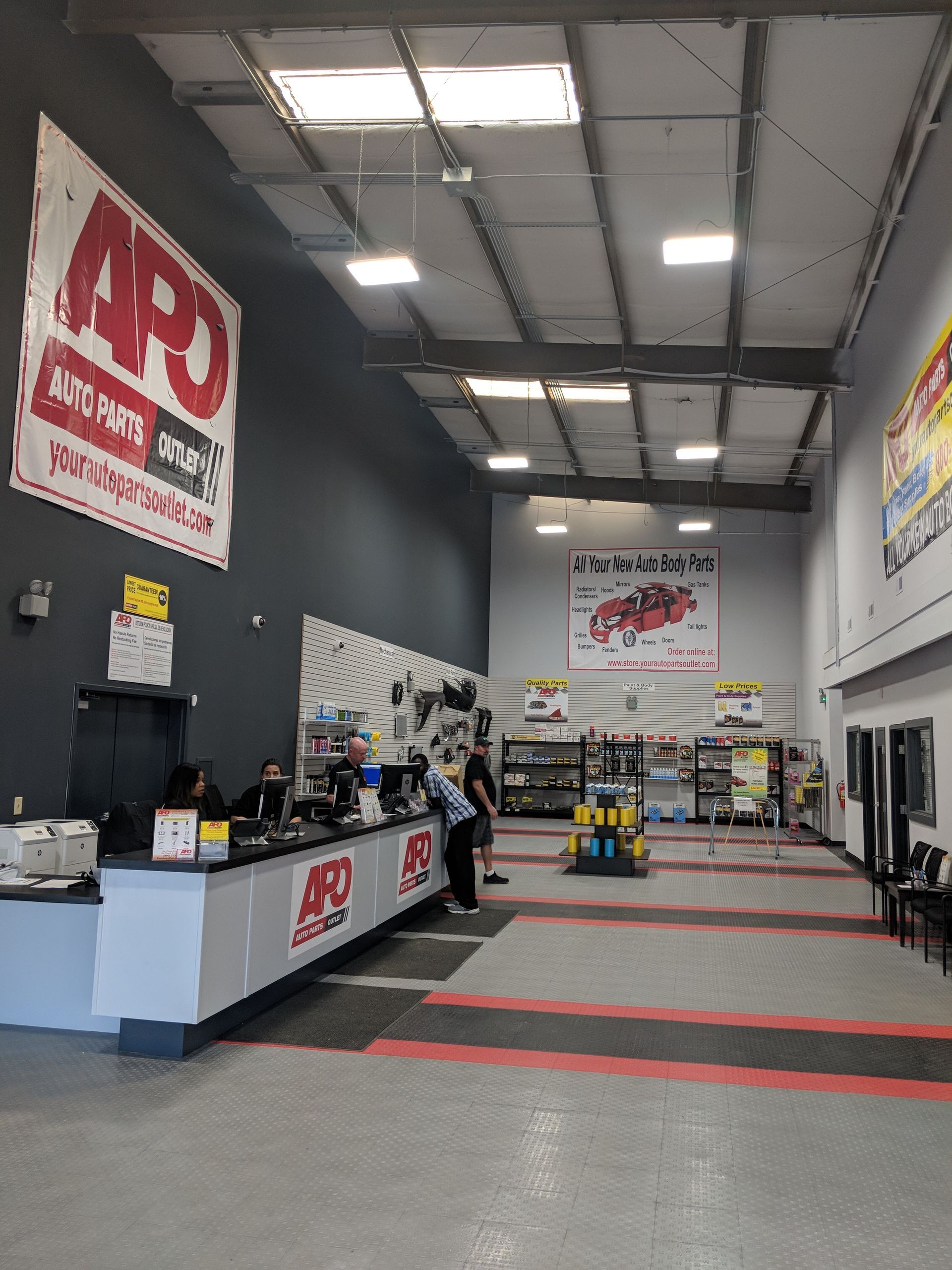 An auto parts store interior with a long service counter, staff, and red and white branding on walls and fixtures.