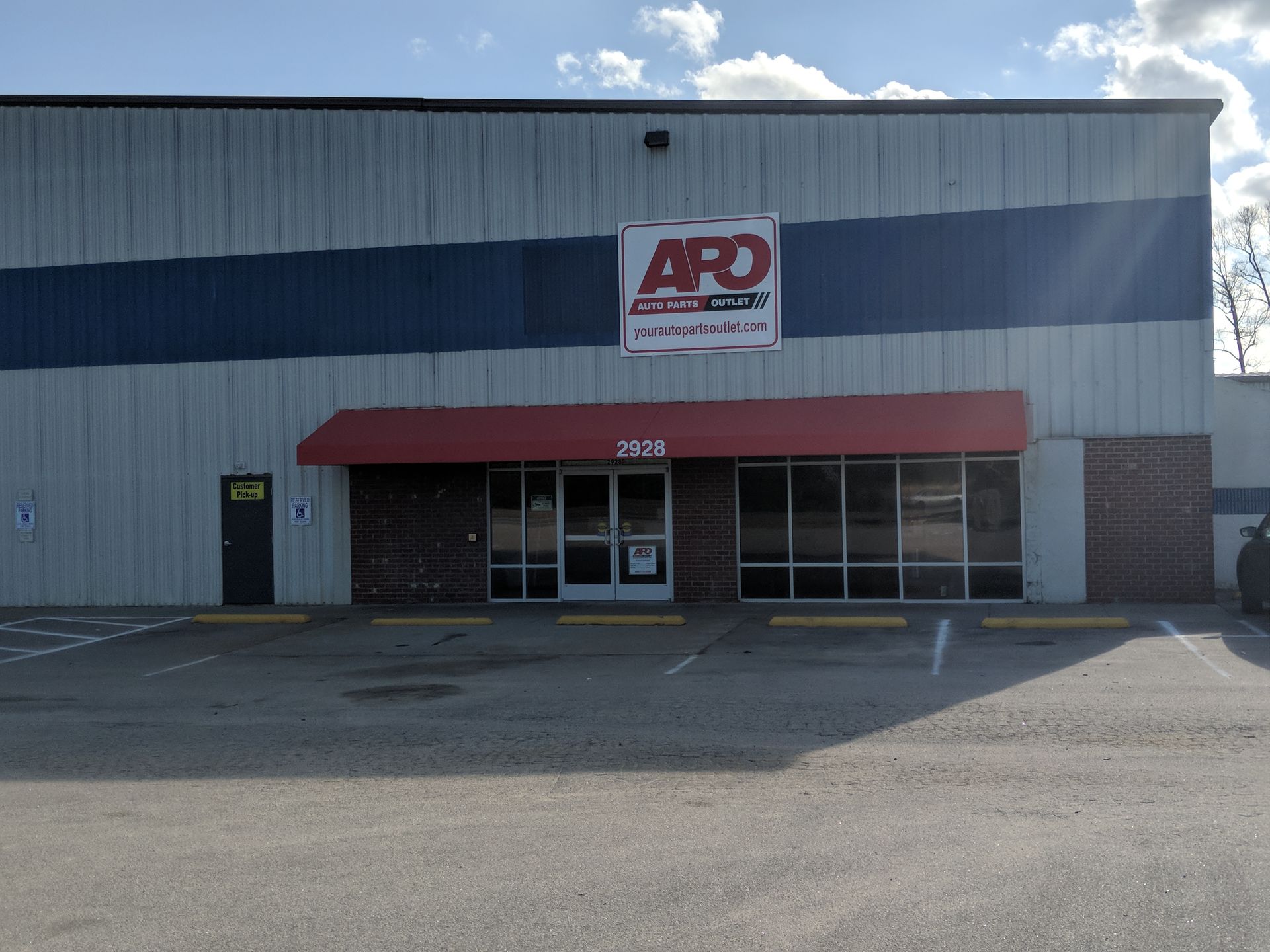 A commercial building with white metal siding, a blue stripe, a red awning, and a sign reading 