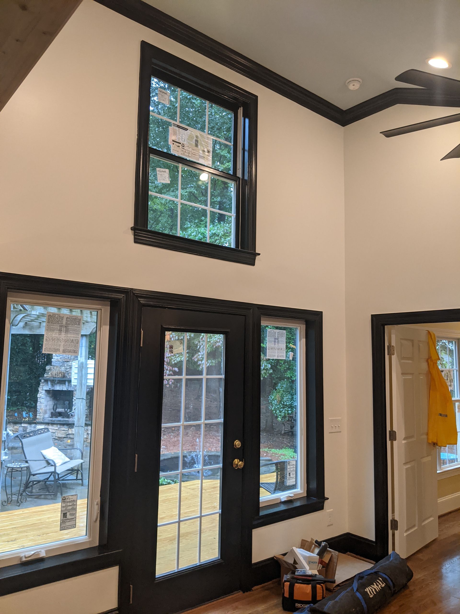 A room interior featuring black-framed windows and a glass door, with white walls and a yellow coat visible in a doorway.