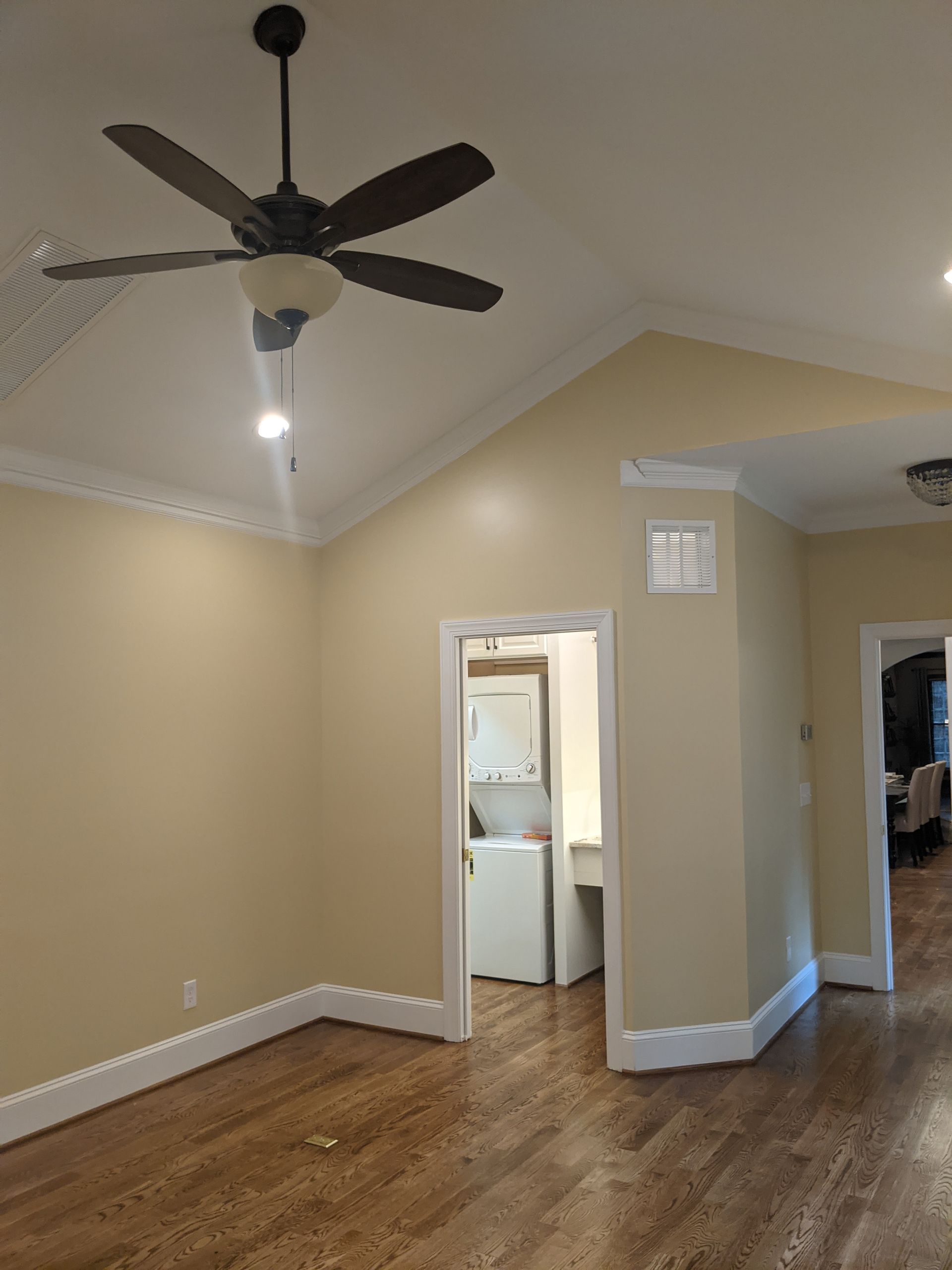 A tan-walled room with vaulted ceilings, a dark ceiling fan, hardwood floors, and doorways leading to other rooms.