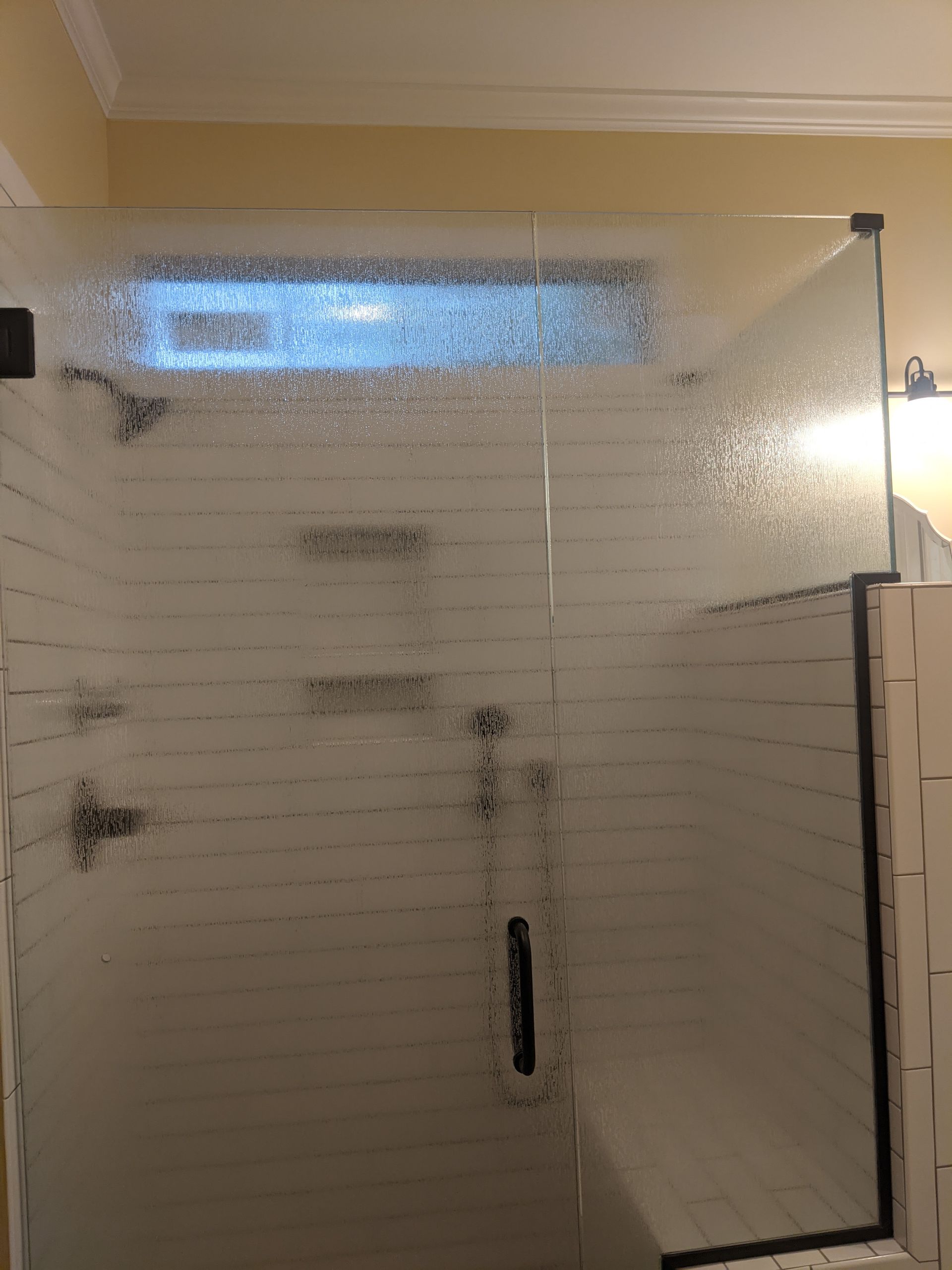 A glass shower door with a frosted, horizontal-line pattern and a top transom window, installed in a tiled bathroom.
