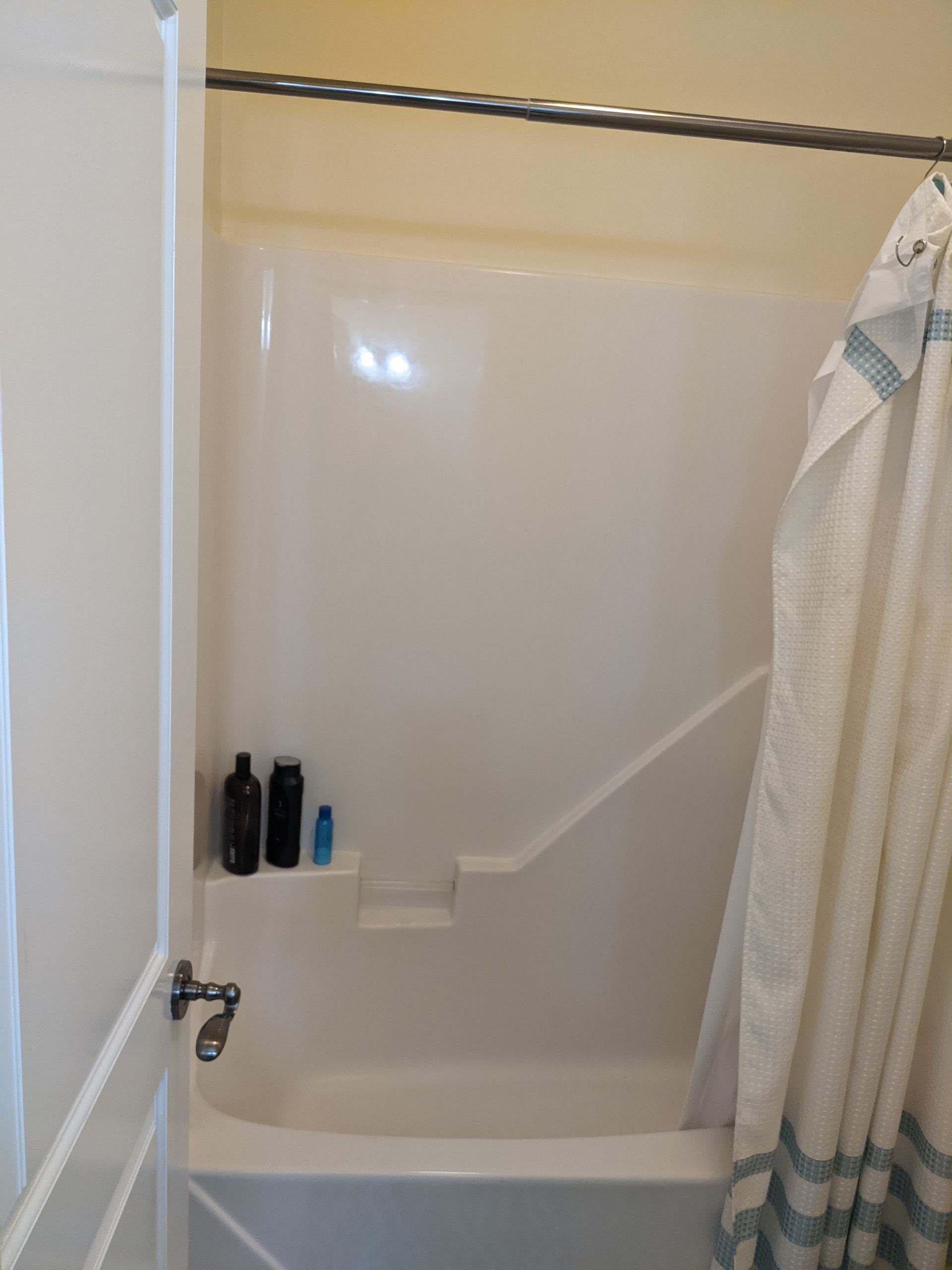 A white shower stall and bathtub with a shower curtain hanging on the right and toiletries on a built-in shelf.
