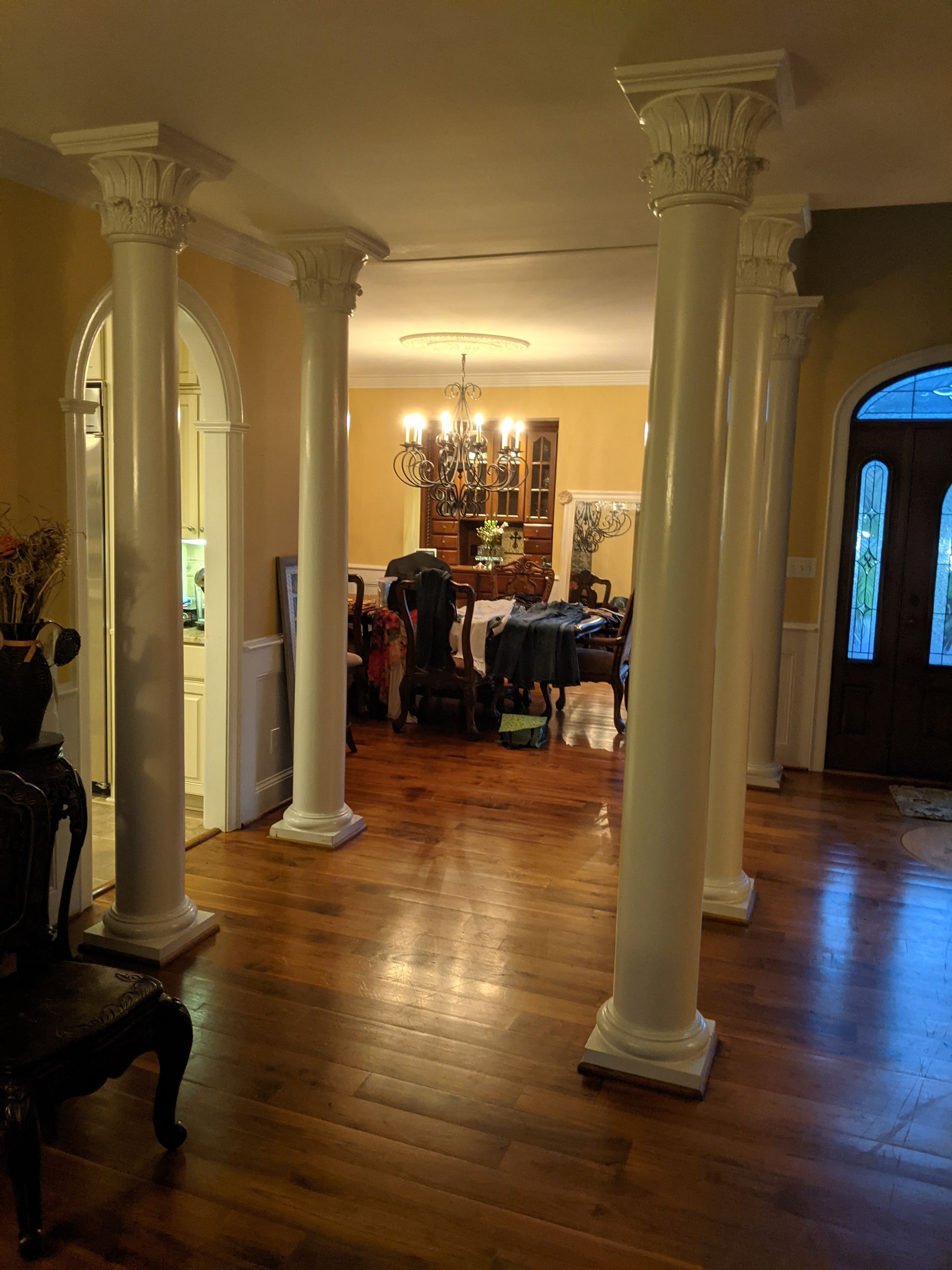 A room interior featuring several white decorative columns leading to a dining area with a chandelier and wooden floor.