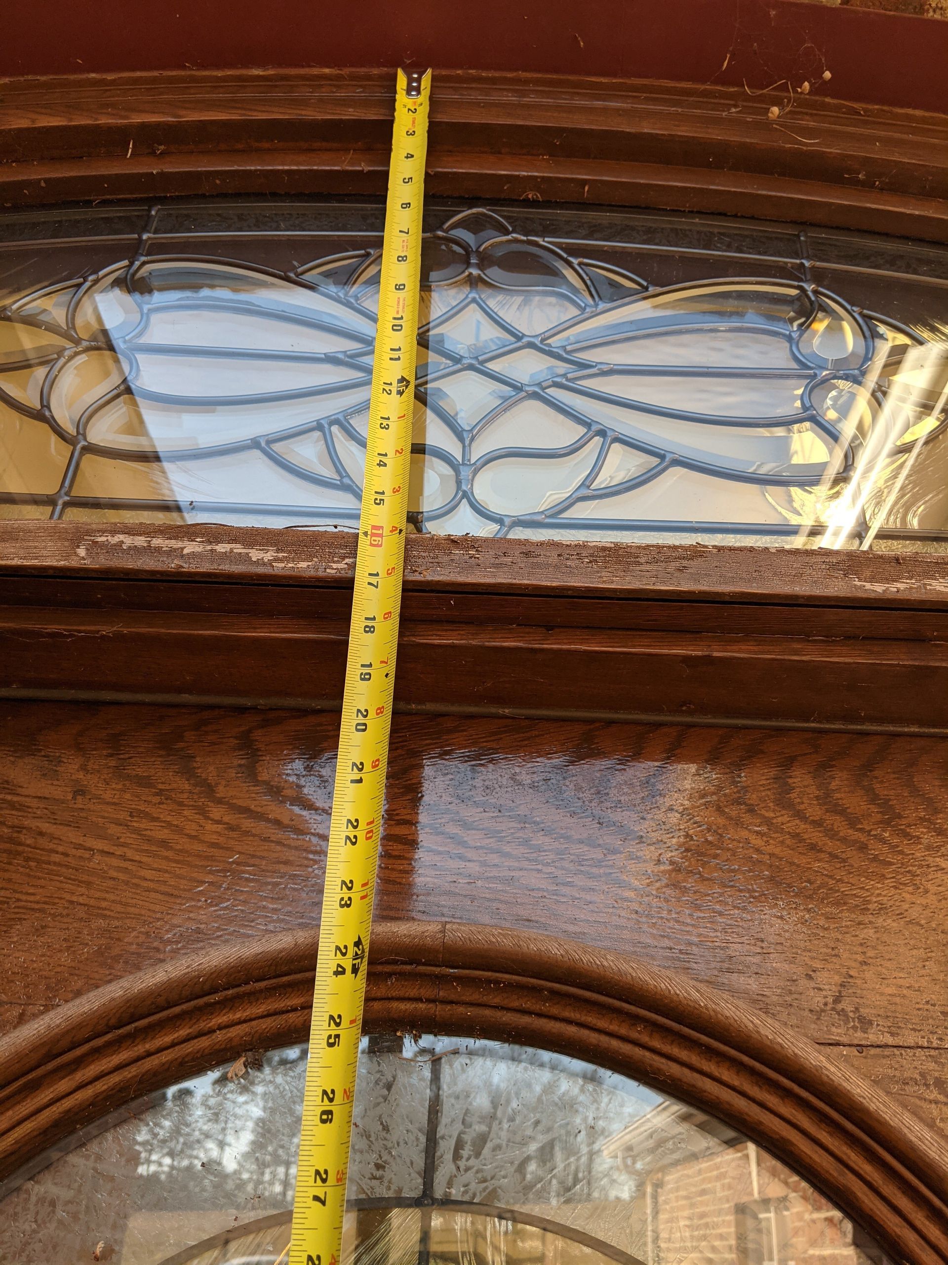A yellow tape measure positioned vertically against a decorative wooden door with two glass panels.