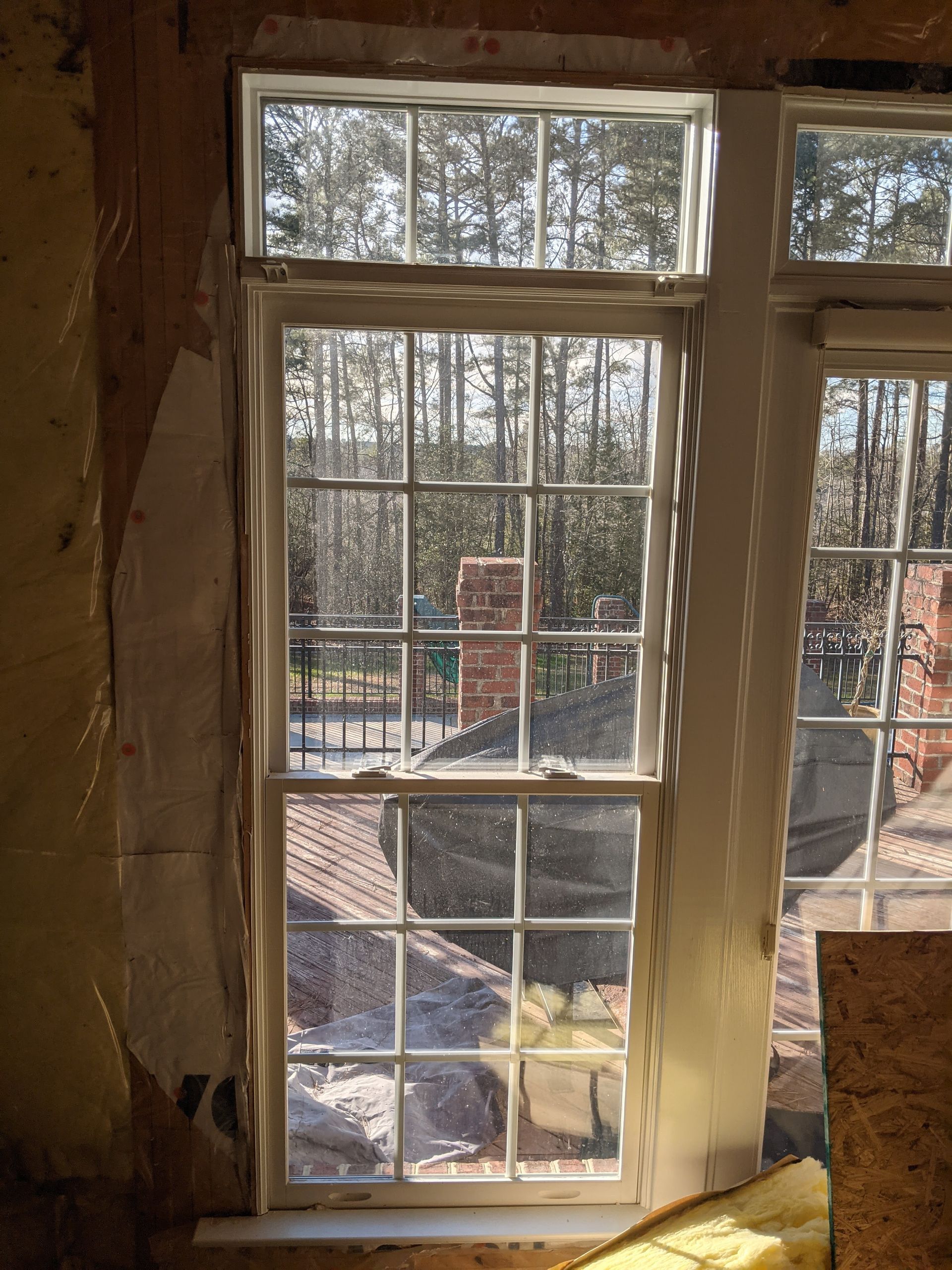 A white-framed window with small rectangular panes looking out onto a wooded area and a brick structure.