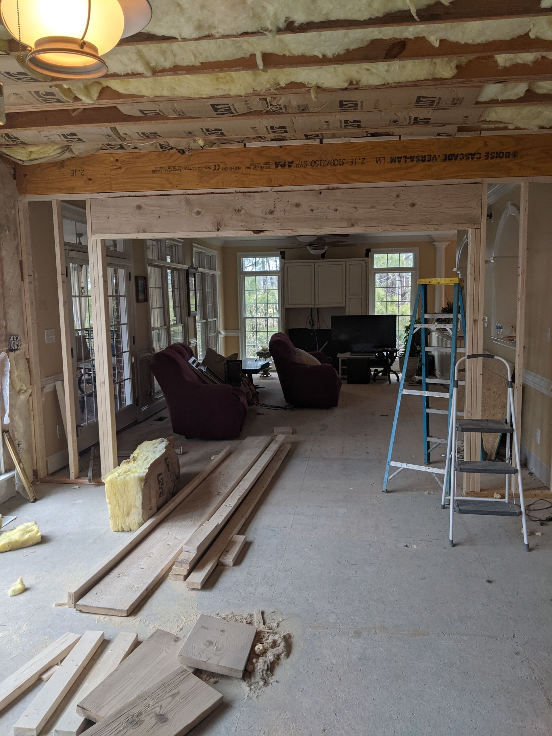Renovating a home interior with a wooden support beam, exposed insulation, a stepladder, and construction materials.