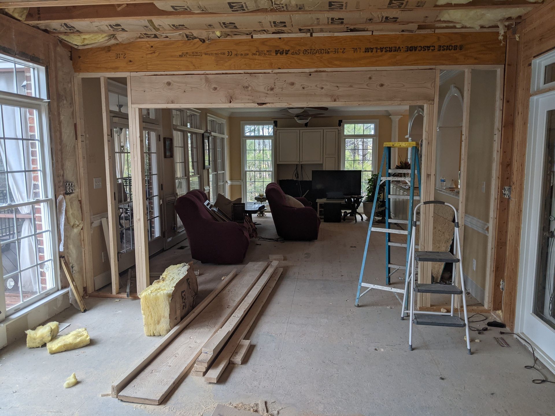 A room under construction with an exposed wooden support beam, wall framing, insulation, and a ladder on a concrete floor.