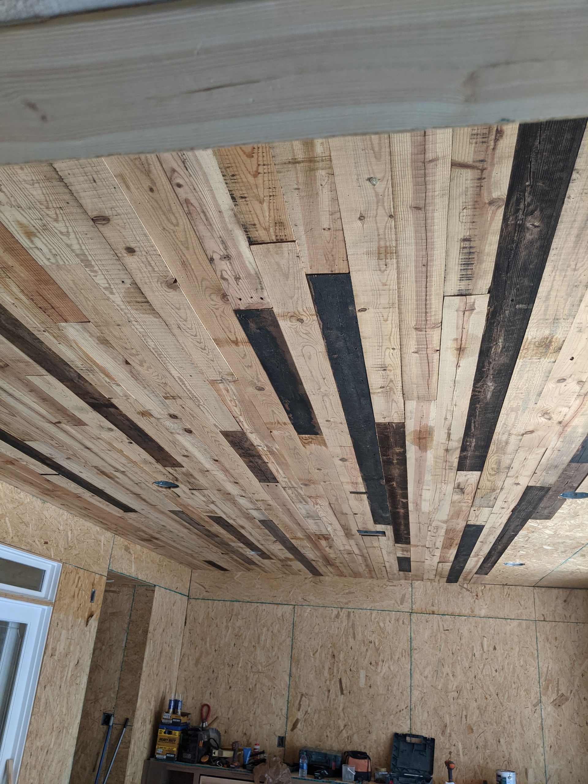 Interior room under construction with OSB walls and a wooden plank ceiling featuring alternating light and dark boards.