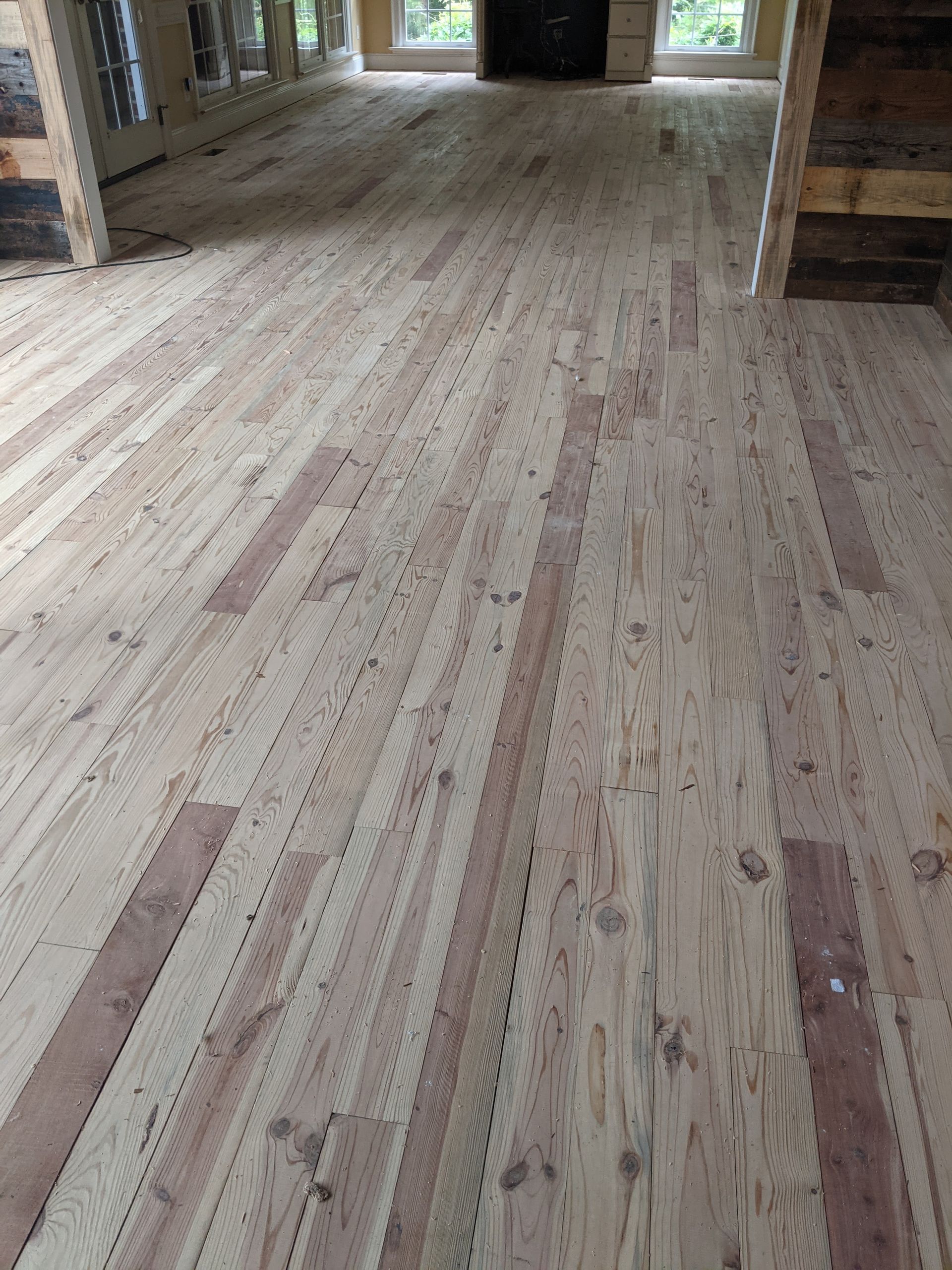 Unfinished light-colored wooden floorboards with dark, textured accent strips installed in a room.