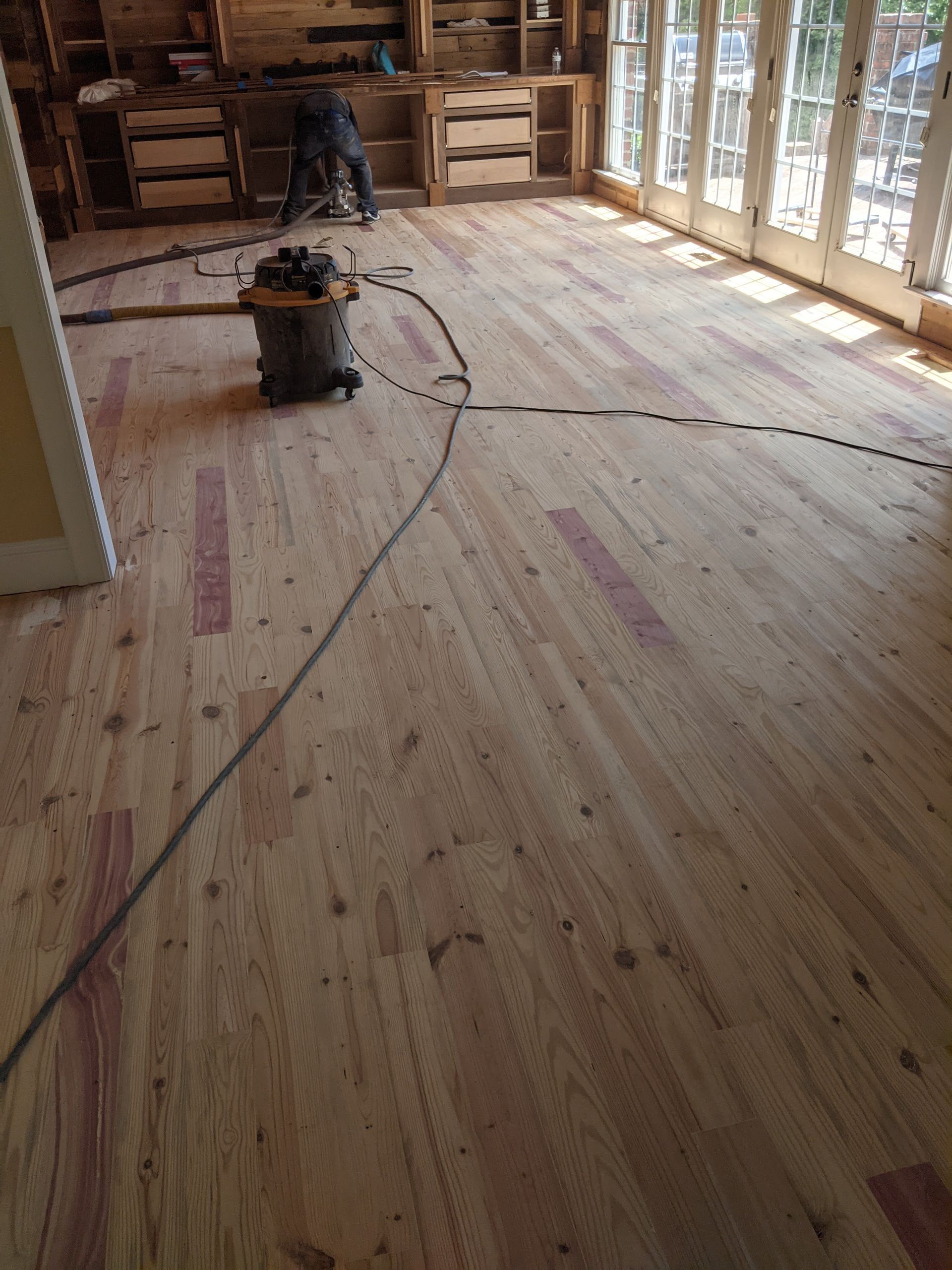 A workshop floor with newly installed wood planks, featuring red markings and a shop vacuum in the foreground.