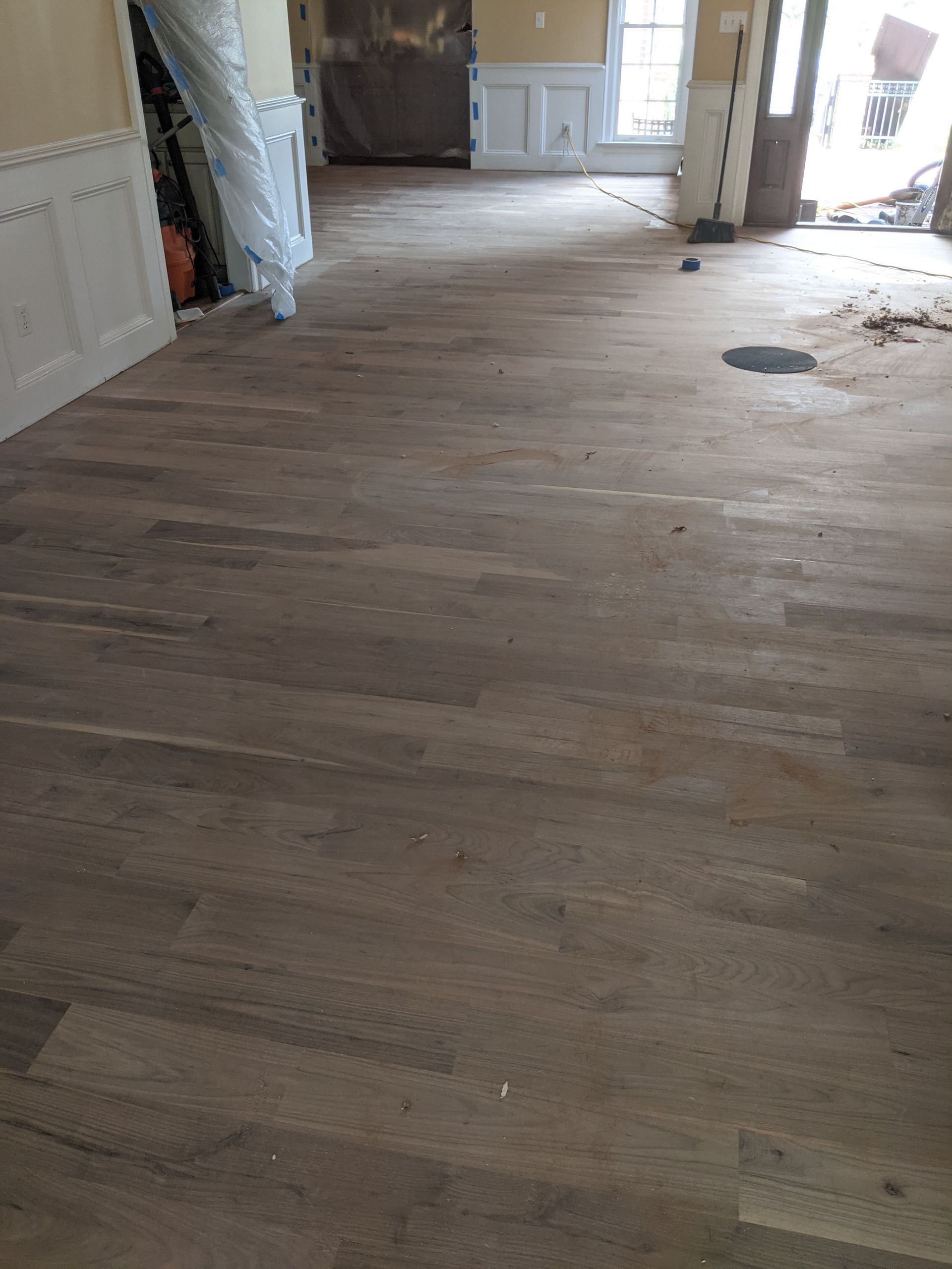 A room with newly installed, light-colored hardwood flooring, white wainscoting, and a doorway leading to another room.