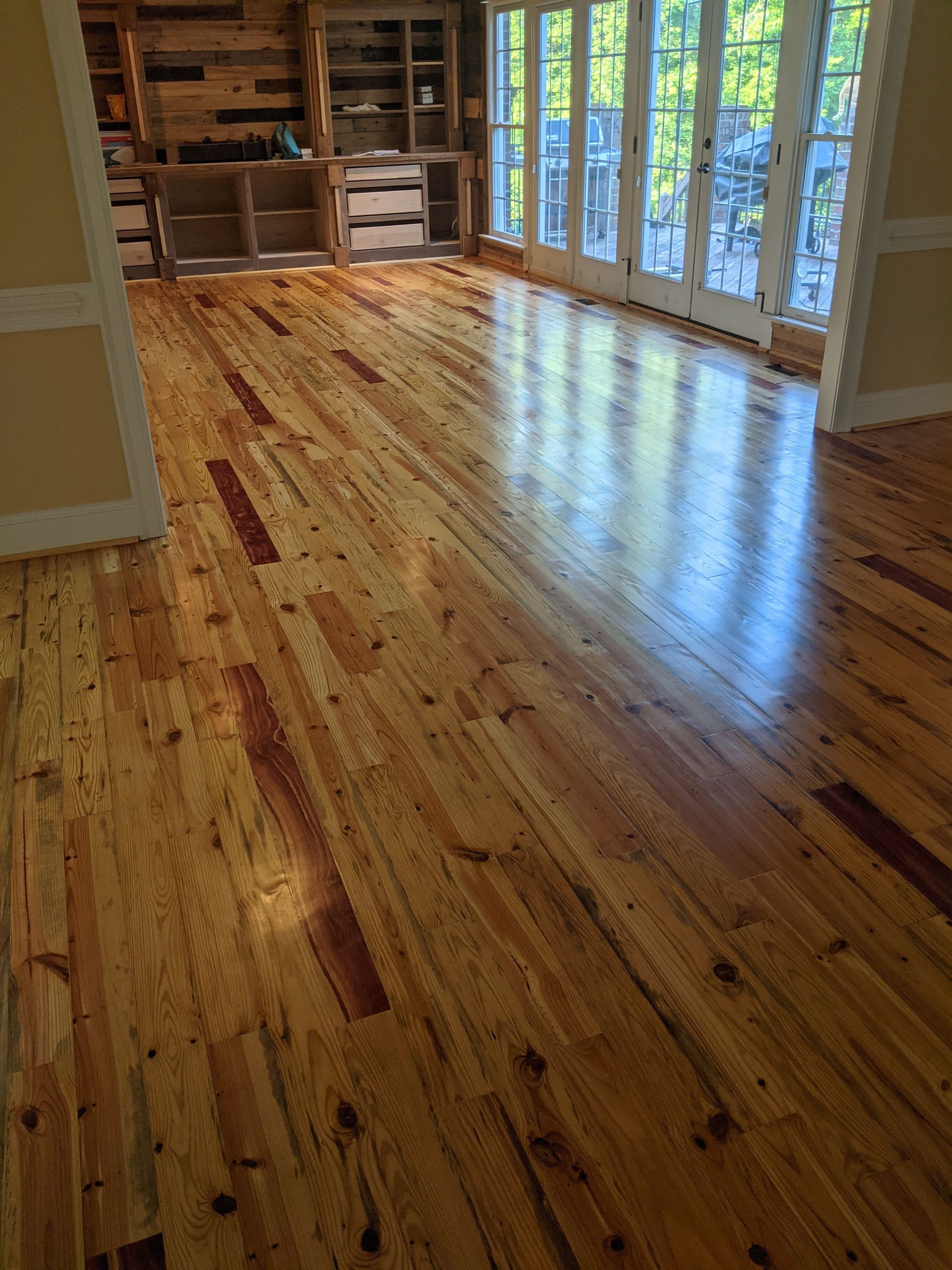 Warm-toned, polished wood floor planks featuring natural knots and grain patterns leading to a room with built-in shelves.