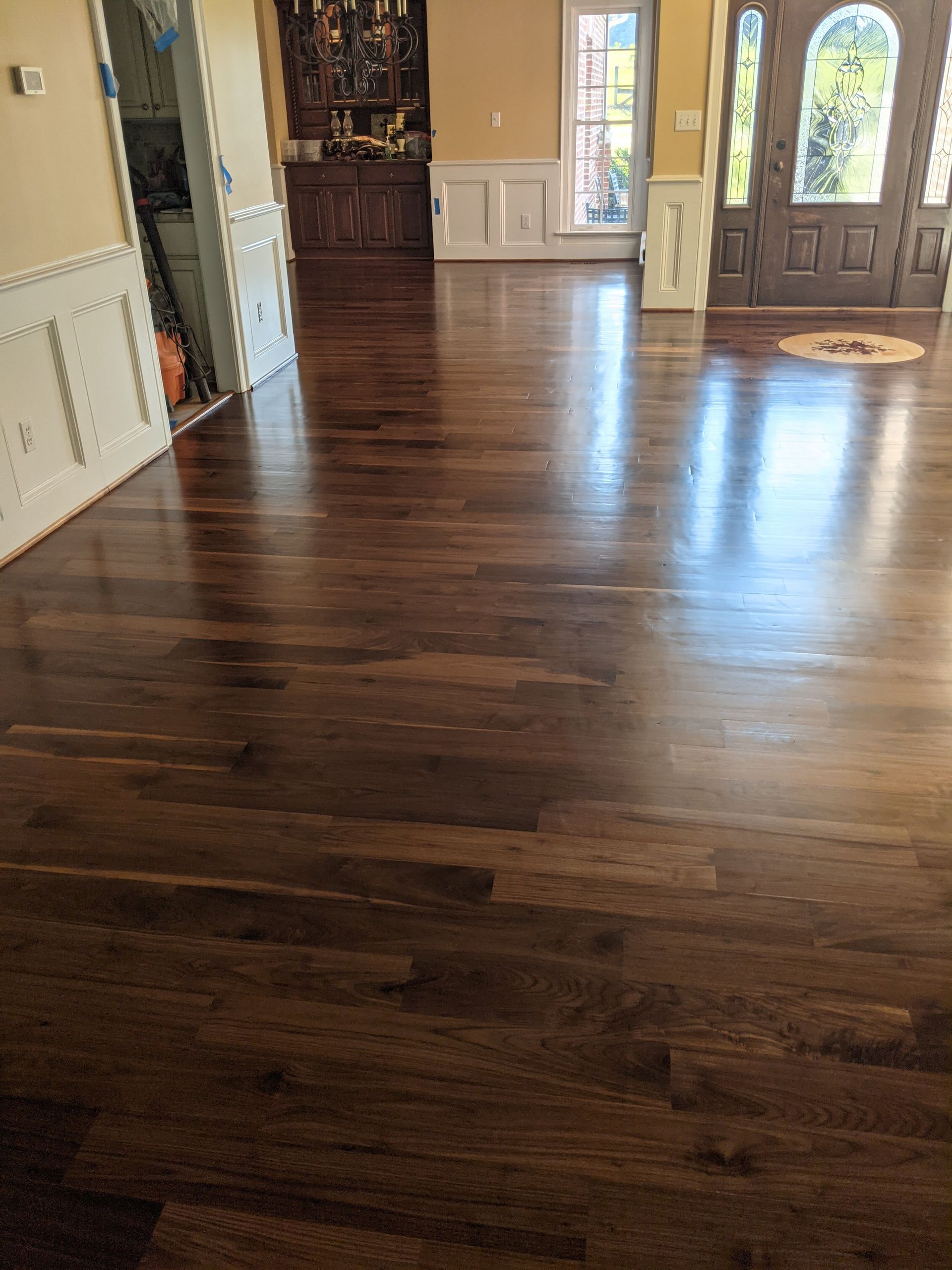 Polished dark hardwood floor in a home entryway with white wainscoting, an arched wooden door, and a small area rug.