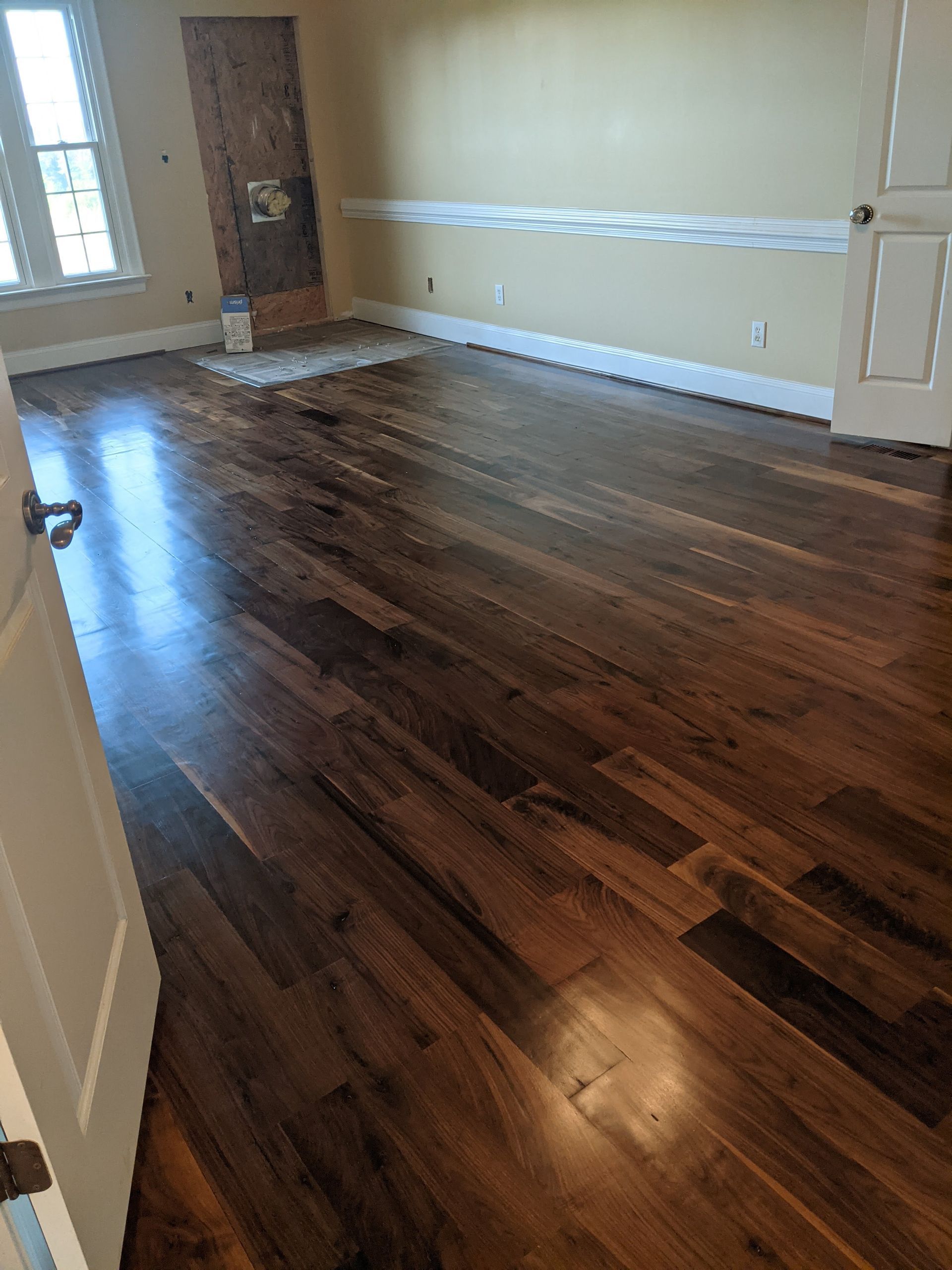 A room with dark brown hardwood flooring, light tan walls, white trim, a closed wooden door, and a bright window.