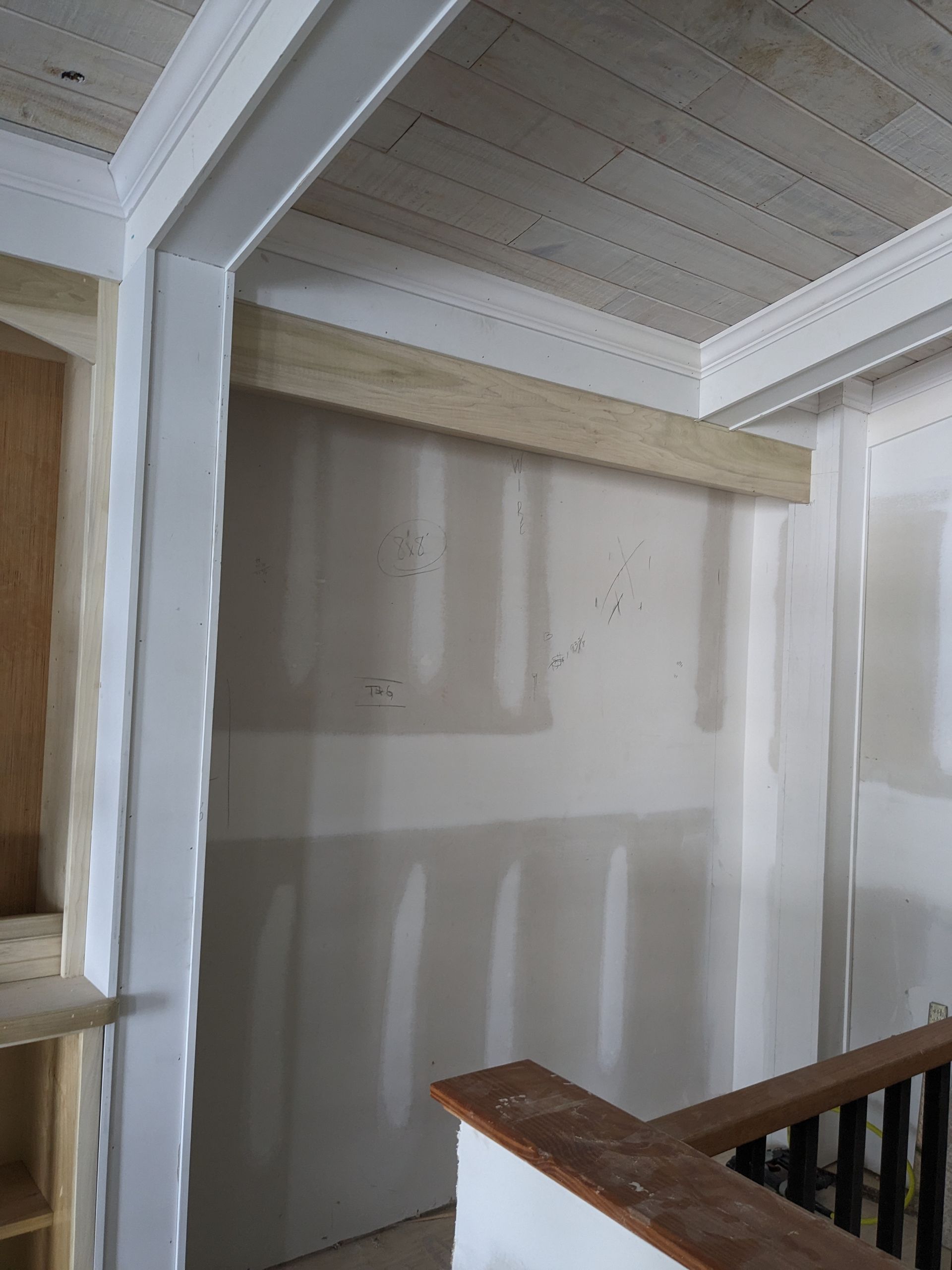 Unfinished interior room with white drywall, wooden support beams, and a partial railing on a staircase landing.
