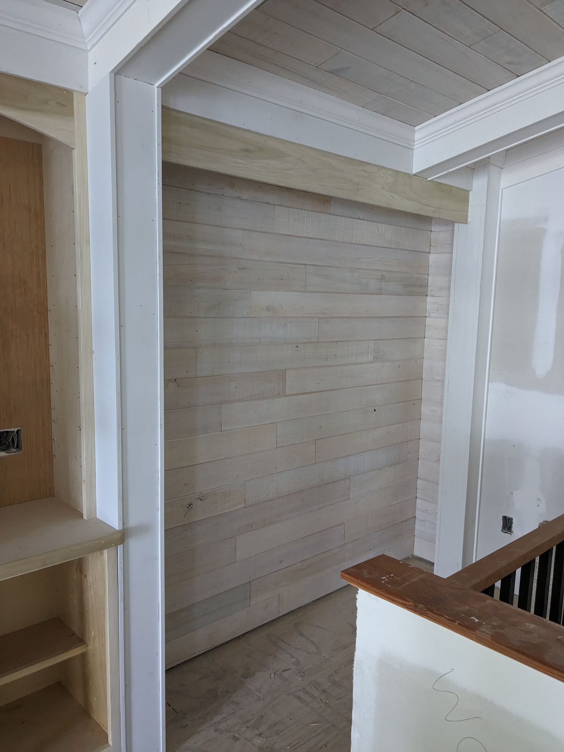 An unfinished interior space with light wood plank wall paneling, white trim, and built-in shelving under construction.